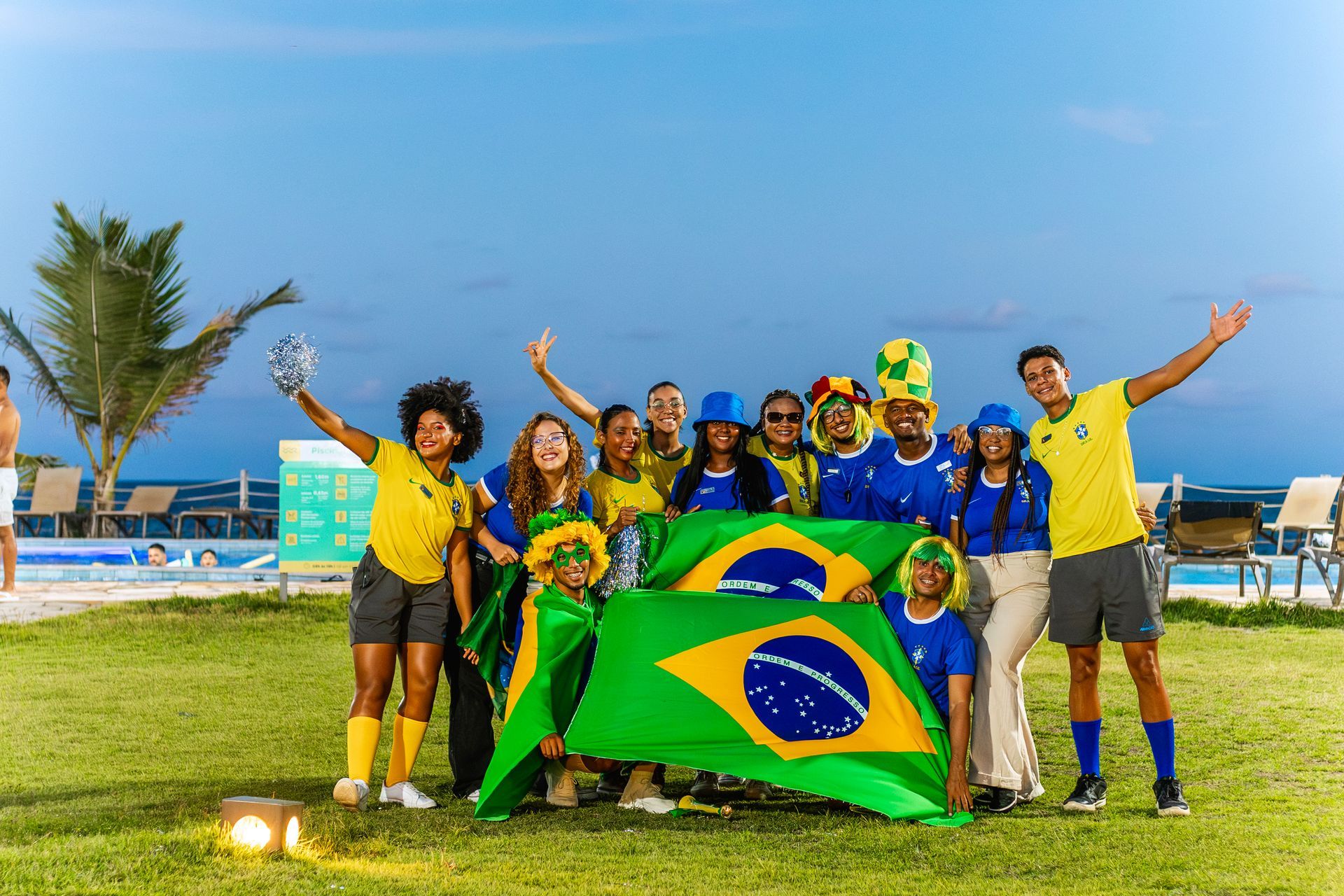 Grupo de pessoas com camisetas do Brasil e bandeiras brasileiras em celebração ao ar livre,.