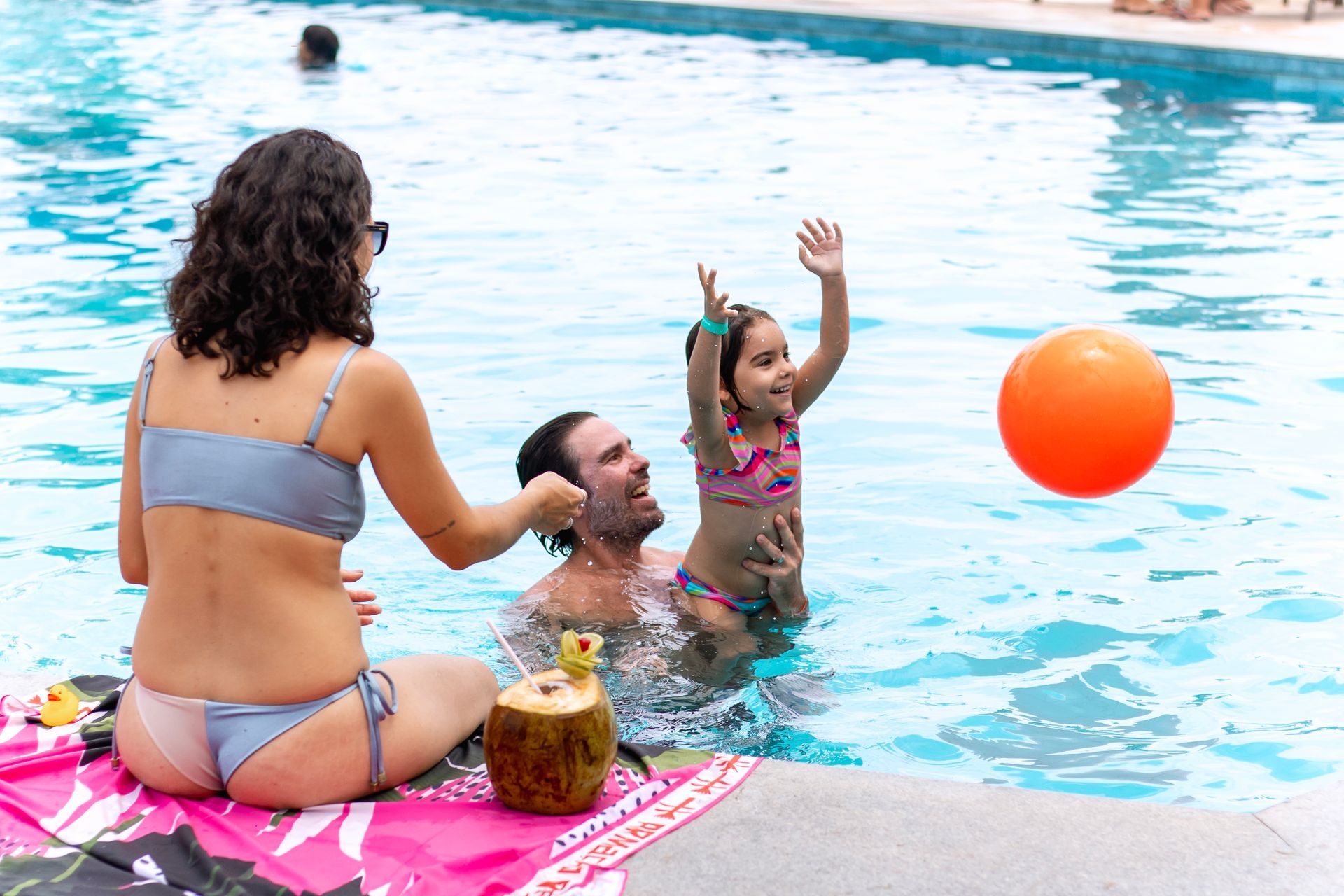 Família curtindo a piscina do Armação Resort em Porto de Galinhas, com criança brincando com bola e coco gelado à beira da piscina