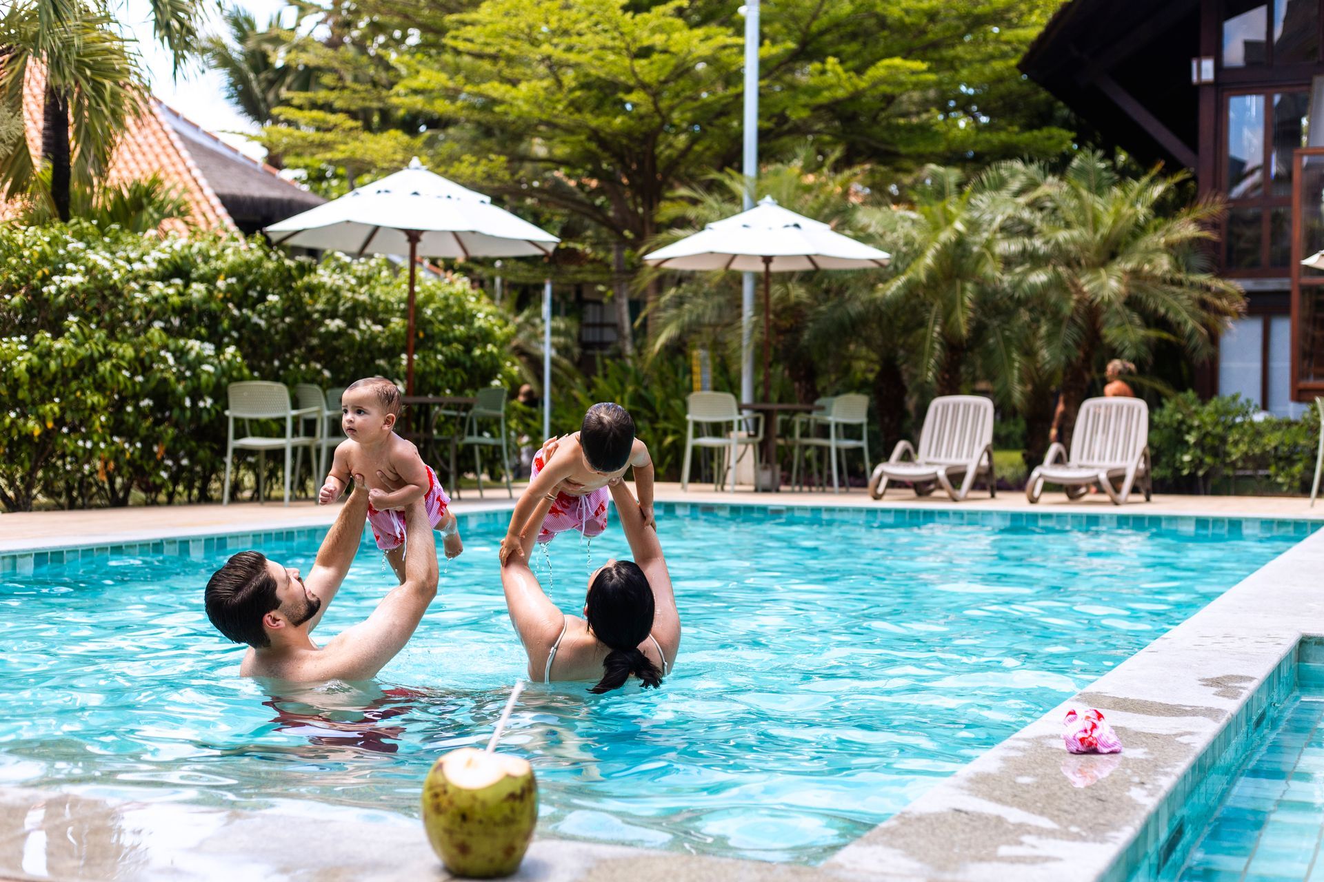 Pais brincam com os filhos pequenos na piscina do resort.