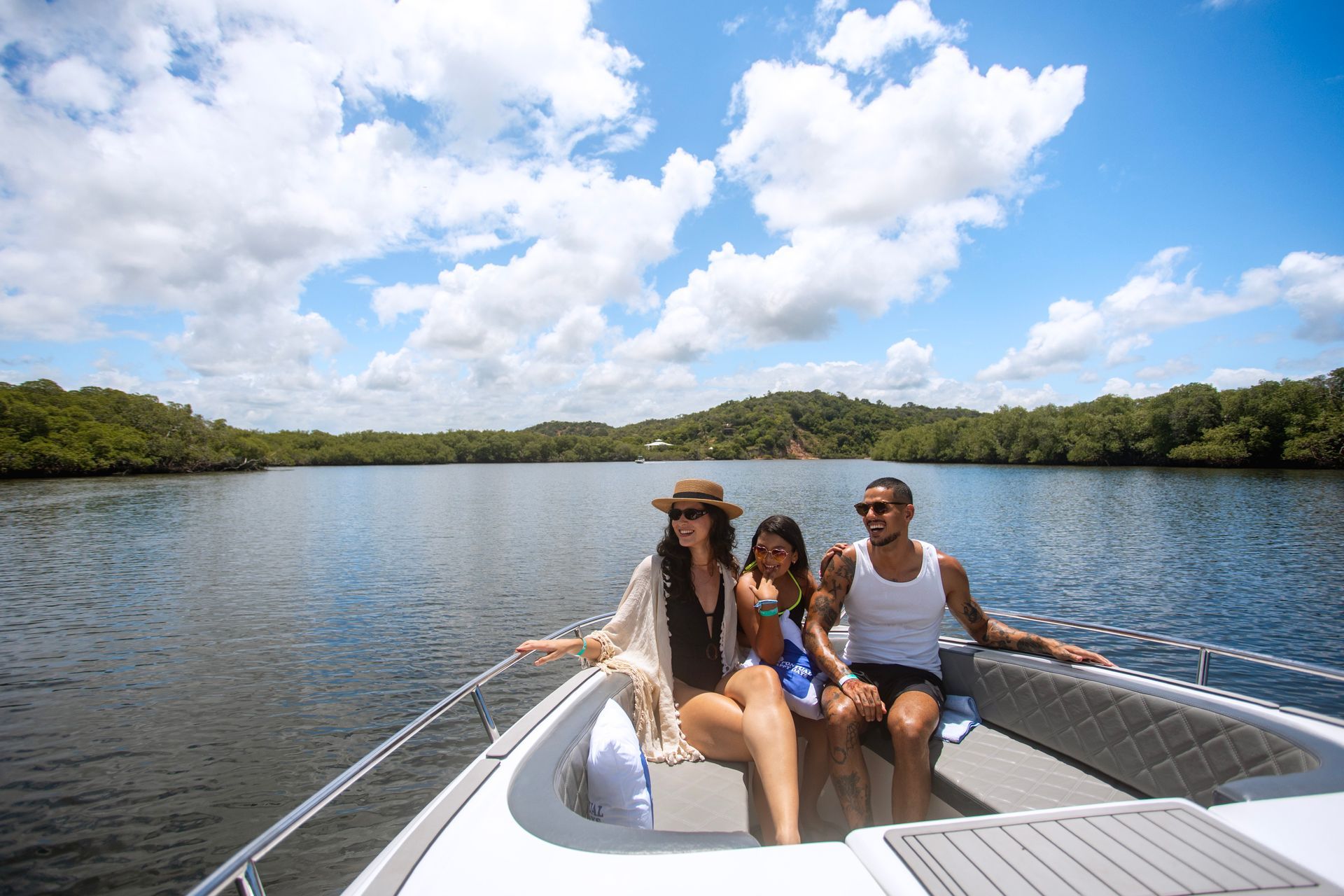 Família relaxando na proa de uma lancha em rio cercado por manguezal.