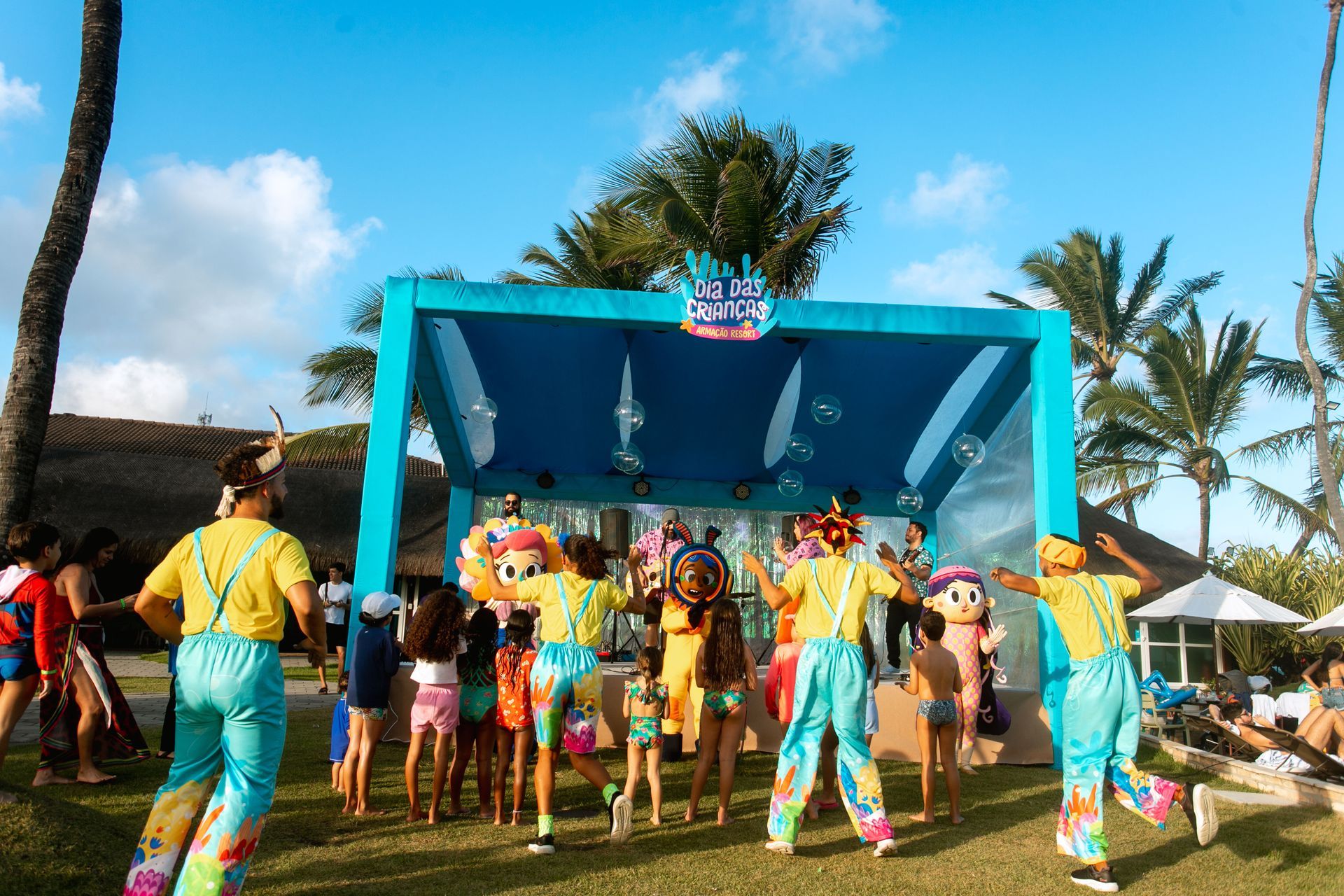 Show de música e apresentações infantis durante o Dia das Crianças no Armação Resort, com palhaços e crianças se divertindo em frente ao palco decorado.