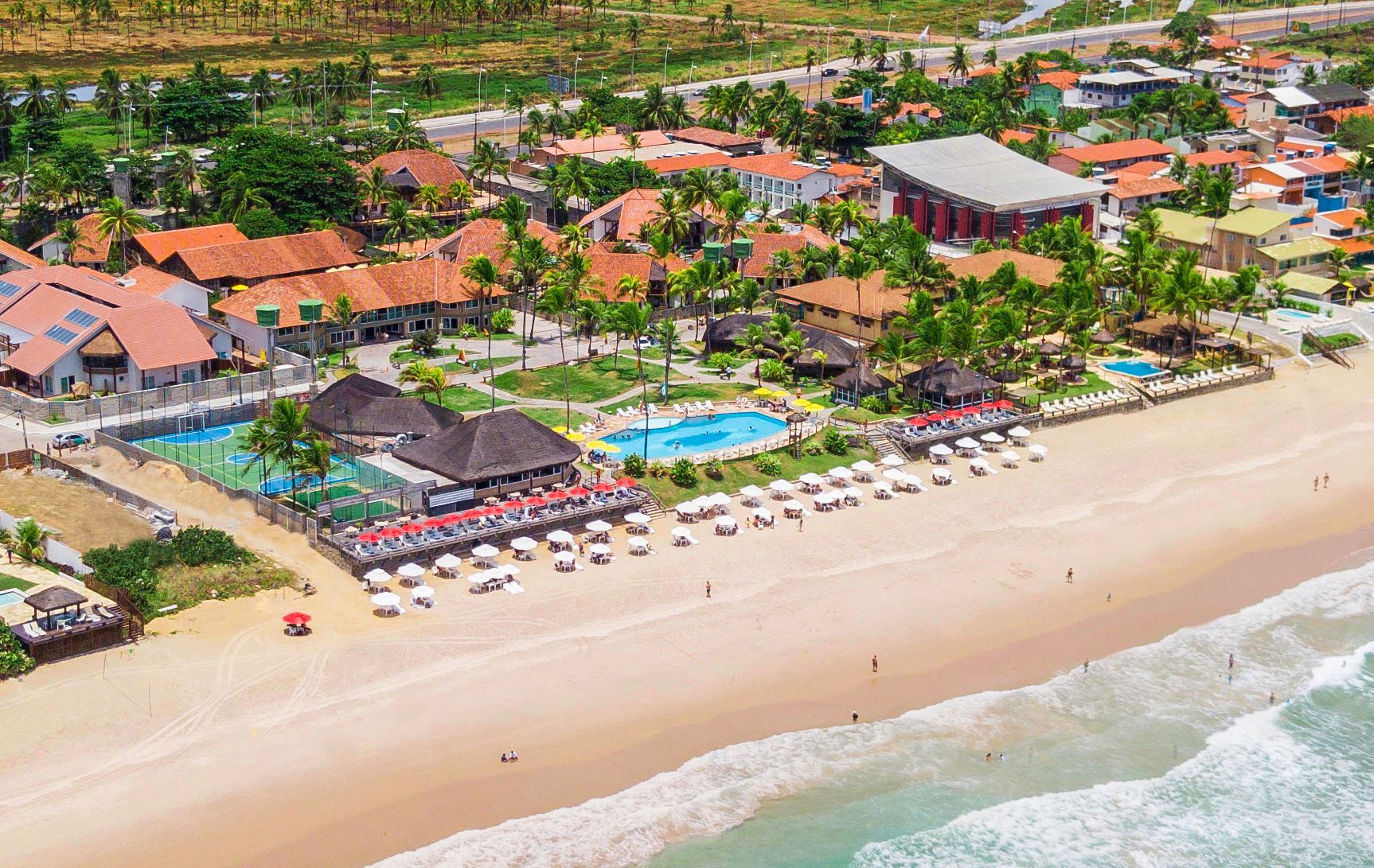Vista aérea do Armação Resort em Porto de Galinhas, mostrando a estrutura do resort à beira-mar, piscinas, áreas de lazer, jardins e a extensa faixa de areia da praia.