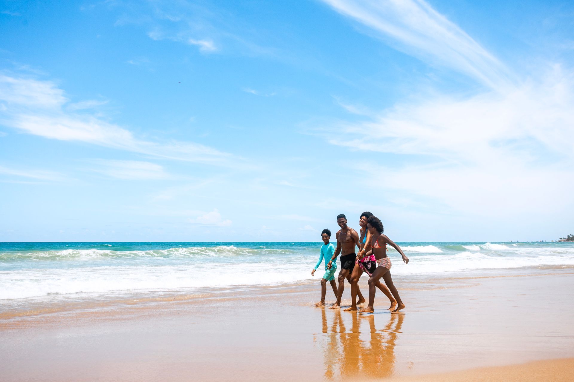 Família caminha pela areia da praia de Porto de Galinhas, com o mar ao fundo.