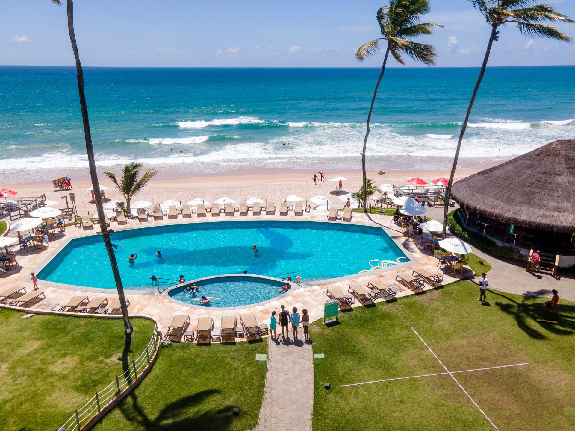 Vista aérea da piscina do Armação Resort com praia, coqueiros & mar azul em Porto de Galinhas.