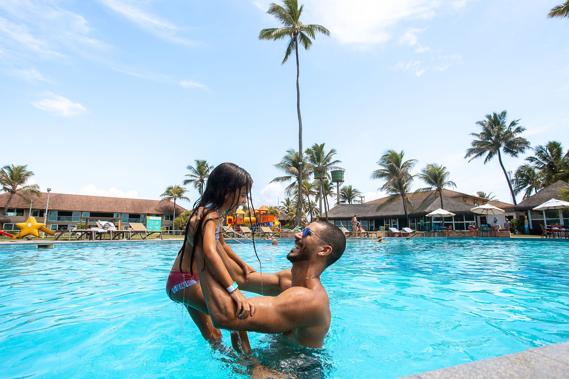 Pai brinca com filha na piscina cercado por coqueiros em dia ensolarado em Porto de Galinhas