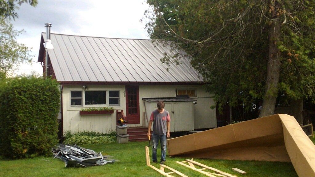 Person standing in a yard beside a house, with a large fallen tree limb on the lawn.
