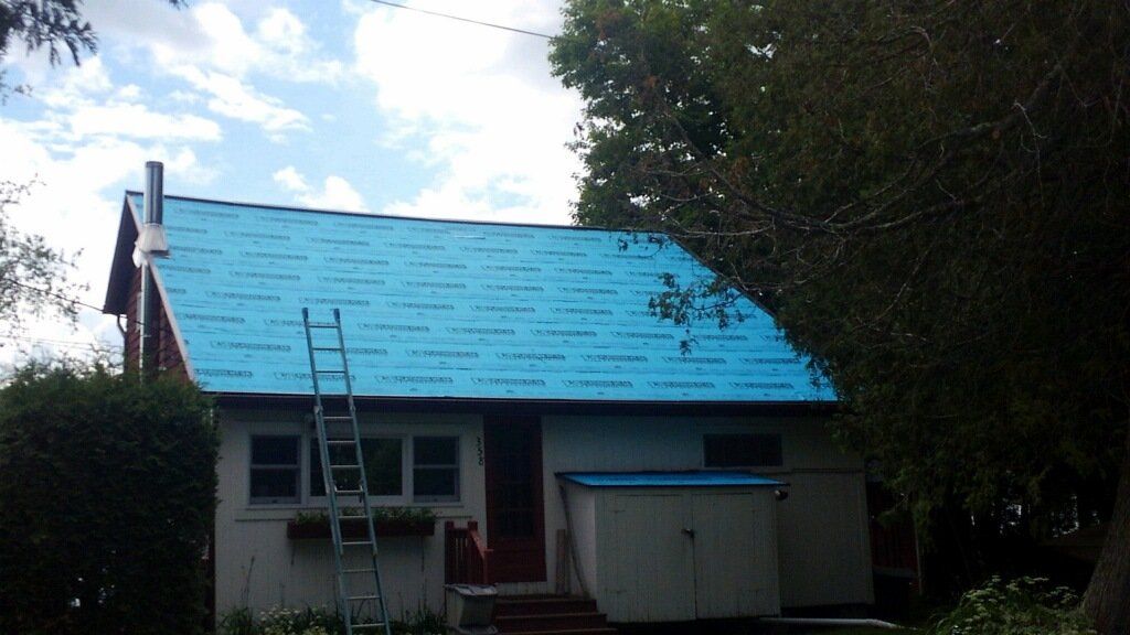 Small house with a bright blue roof, a ladder leaning against it, and a partly cloudy sky.