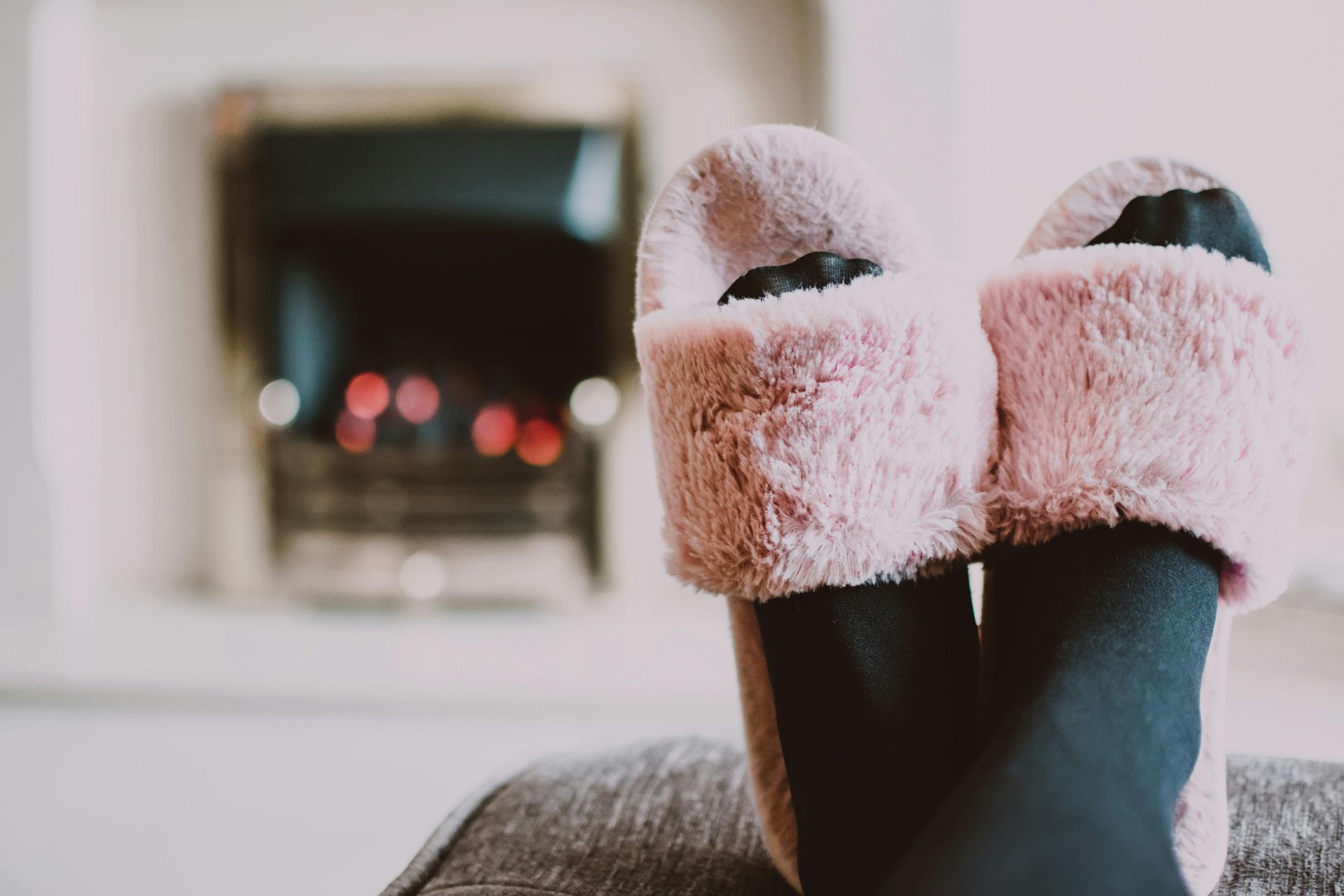 Feet in pink fluffy slippers, resting near a fireplace with a blurred red glow.