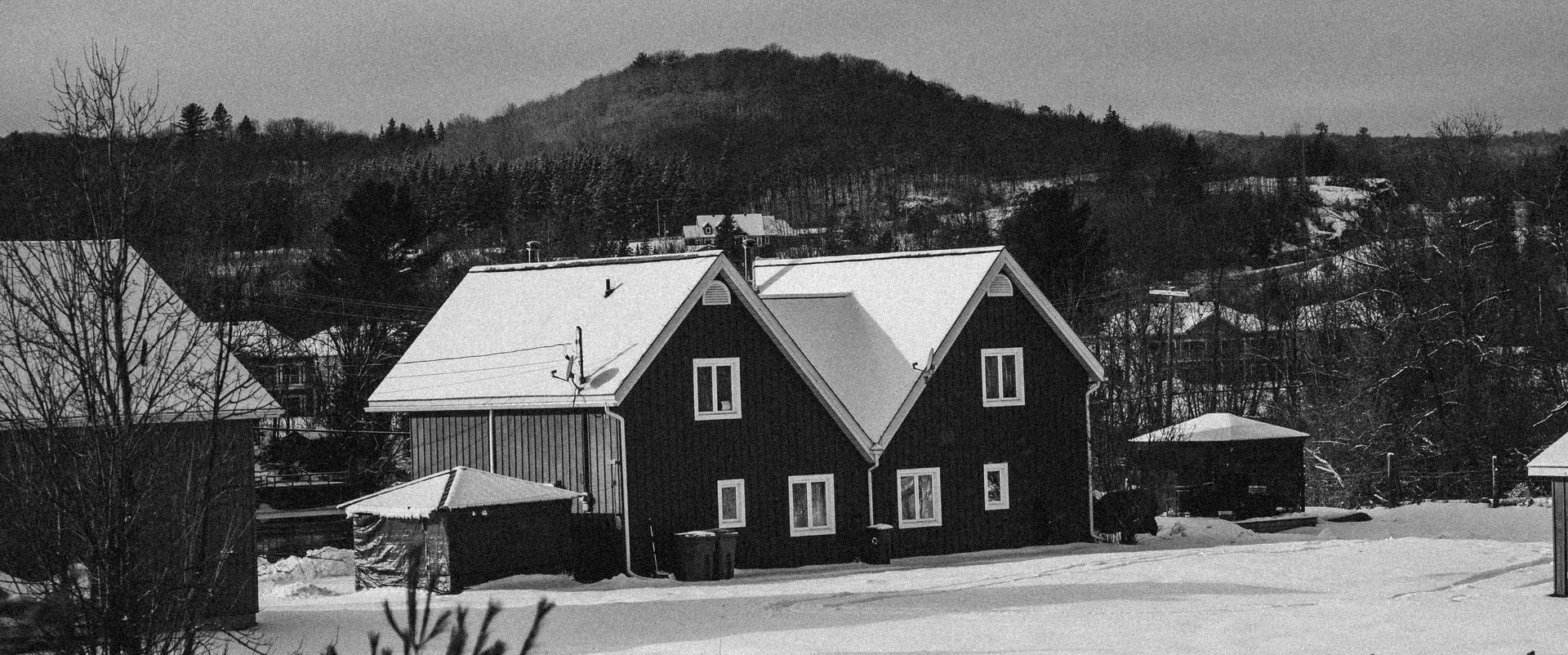 Black-and-white photo of a snow-covered Vermont farmhouse with hills and trees in the background.