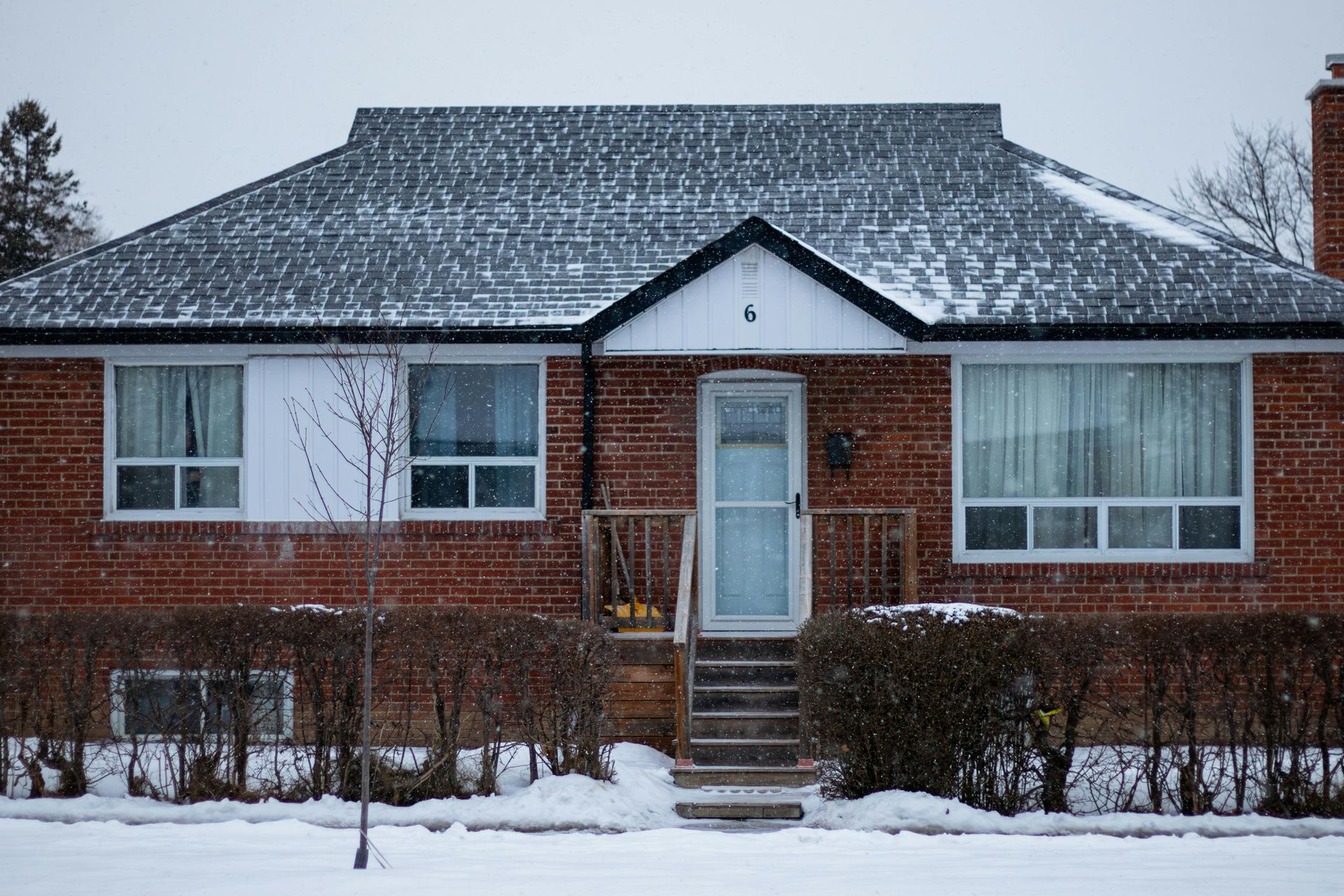 Red brick house in winter, covered with snow, with snow falling.