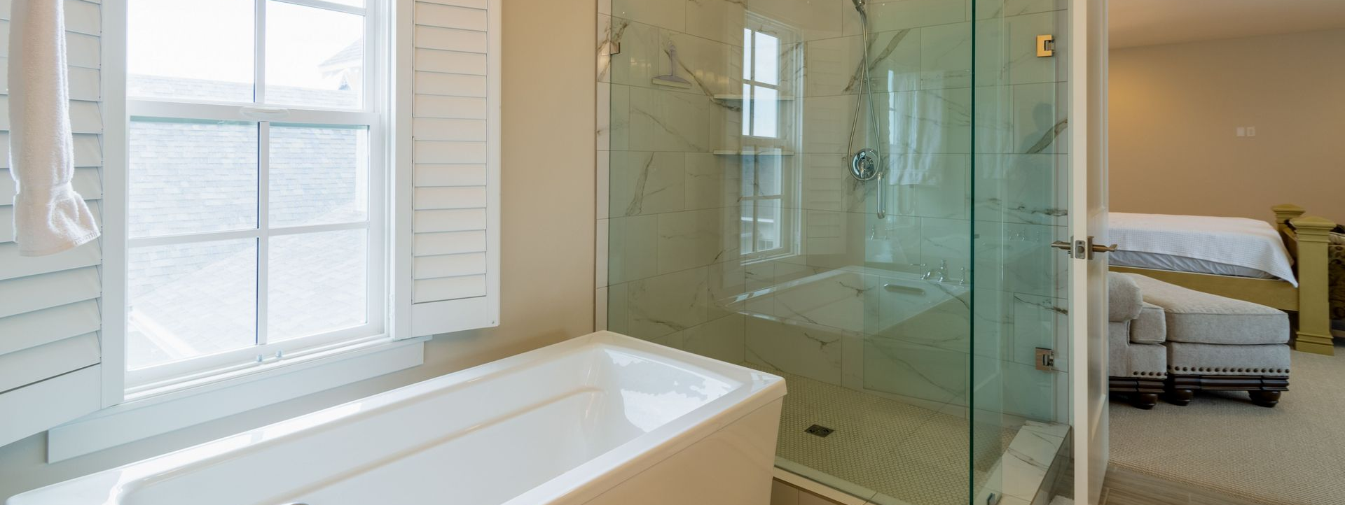Bright guest suite bathroom with soaking tub, glass shower, and bedroom beyond.