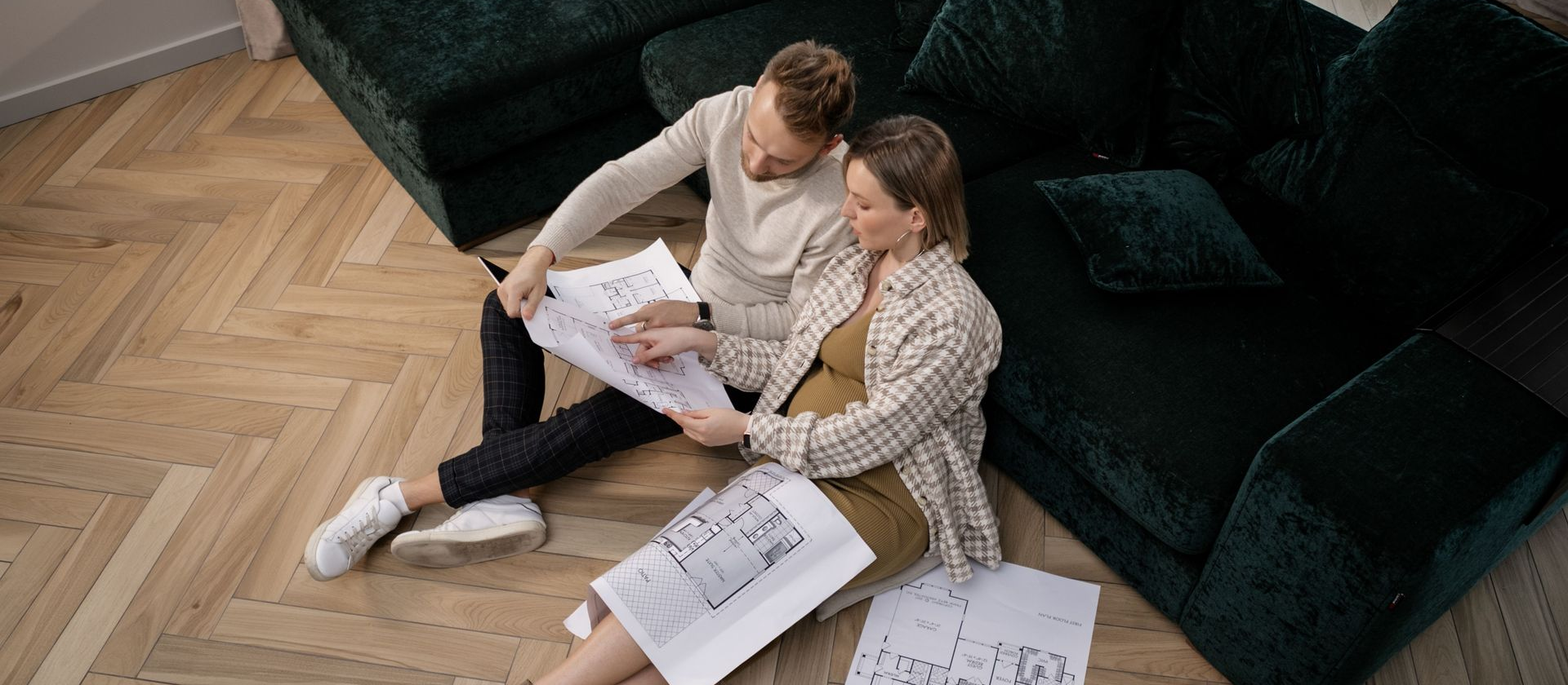 Two people sitting on the floor reviewing custom home floor plans in a living room.