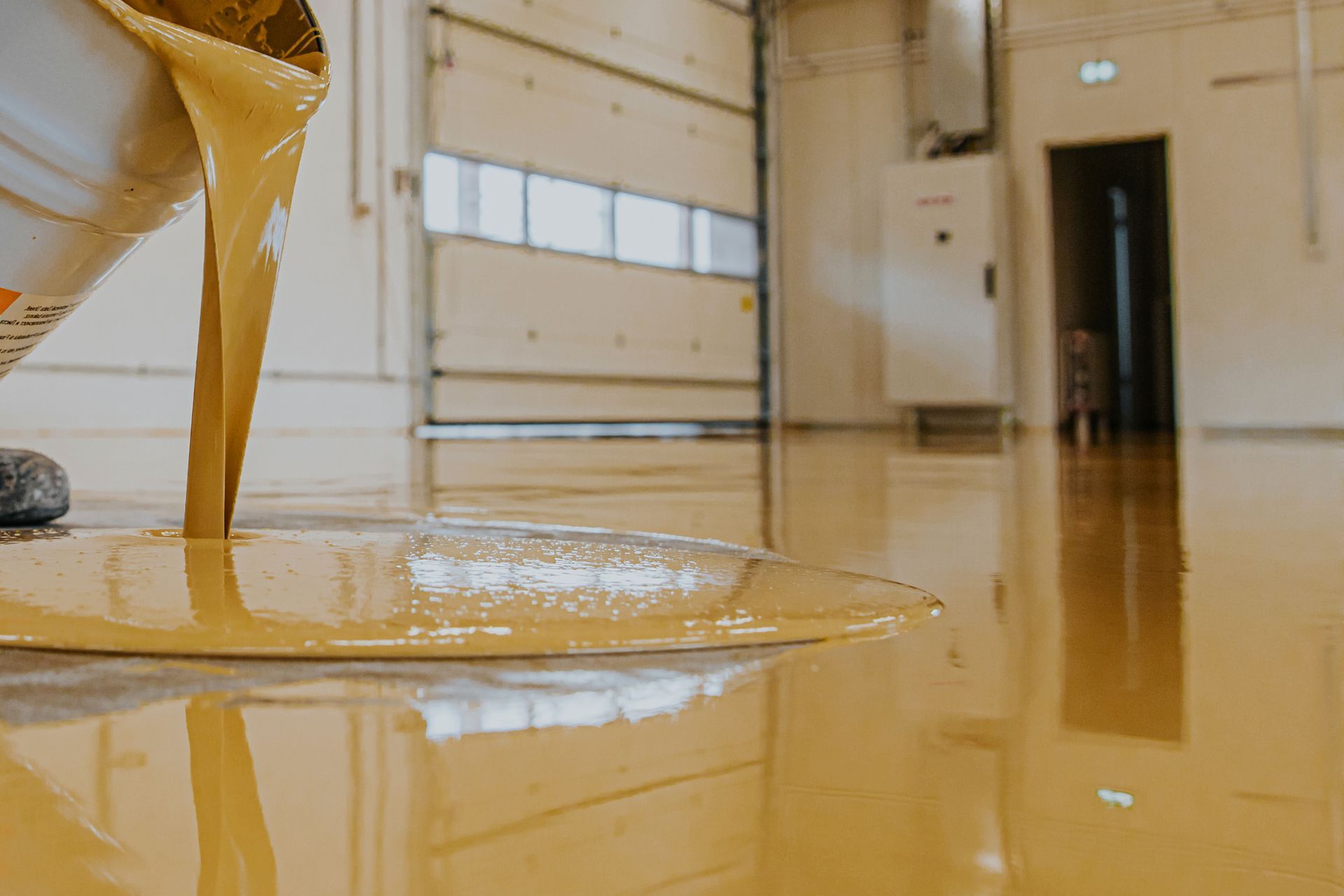 Worker coating garage floor with self-leveling epoxy resin