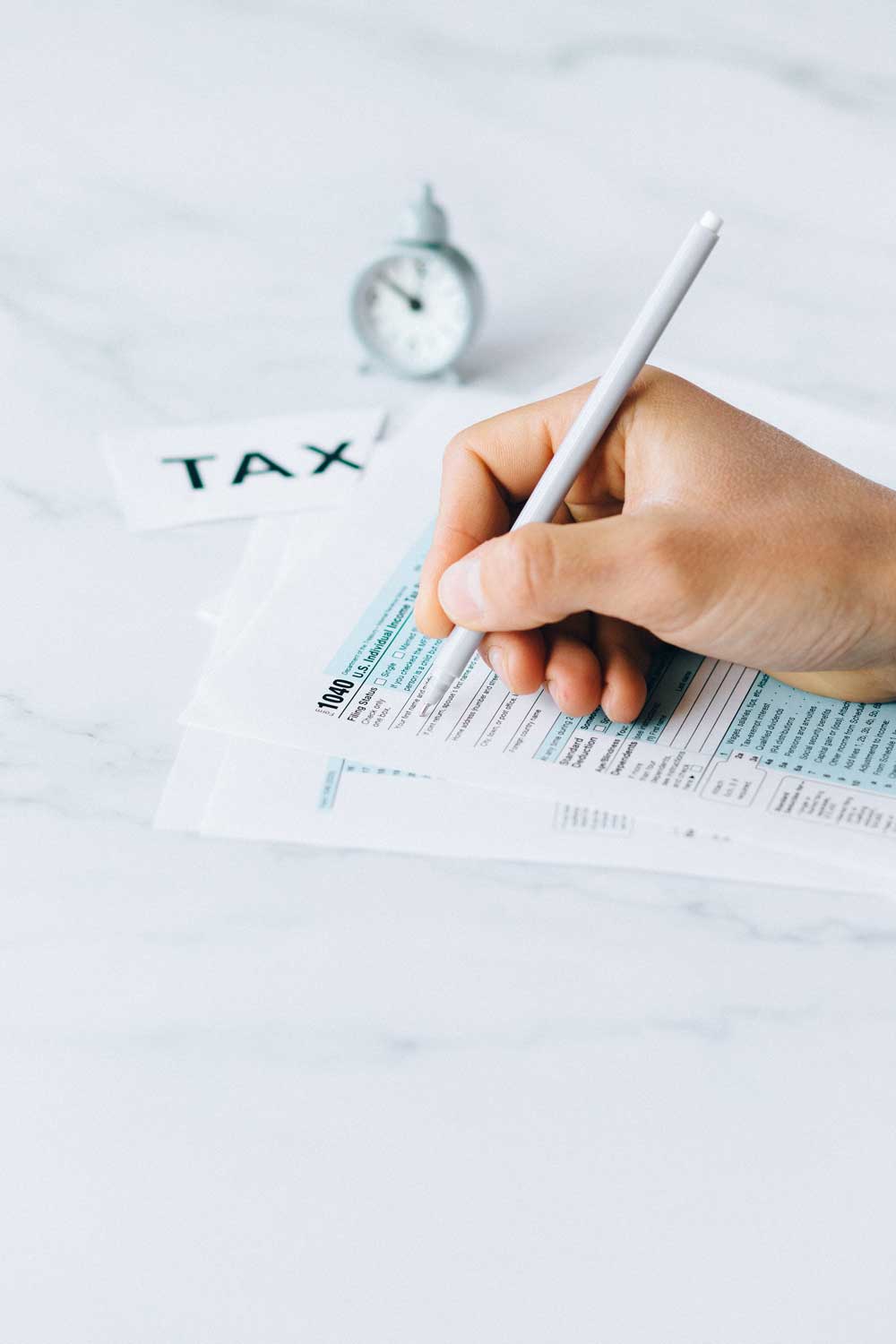 A person is writing on a tax form with a pen.