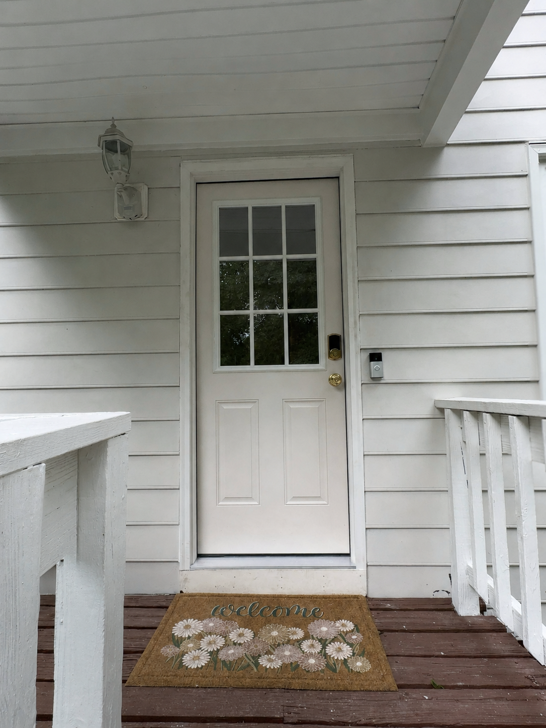 White front door on a house porch with white siding, wooden railings, and a brown doormat.