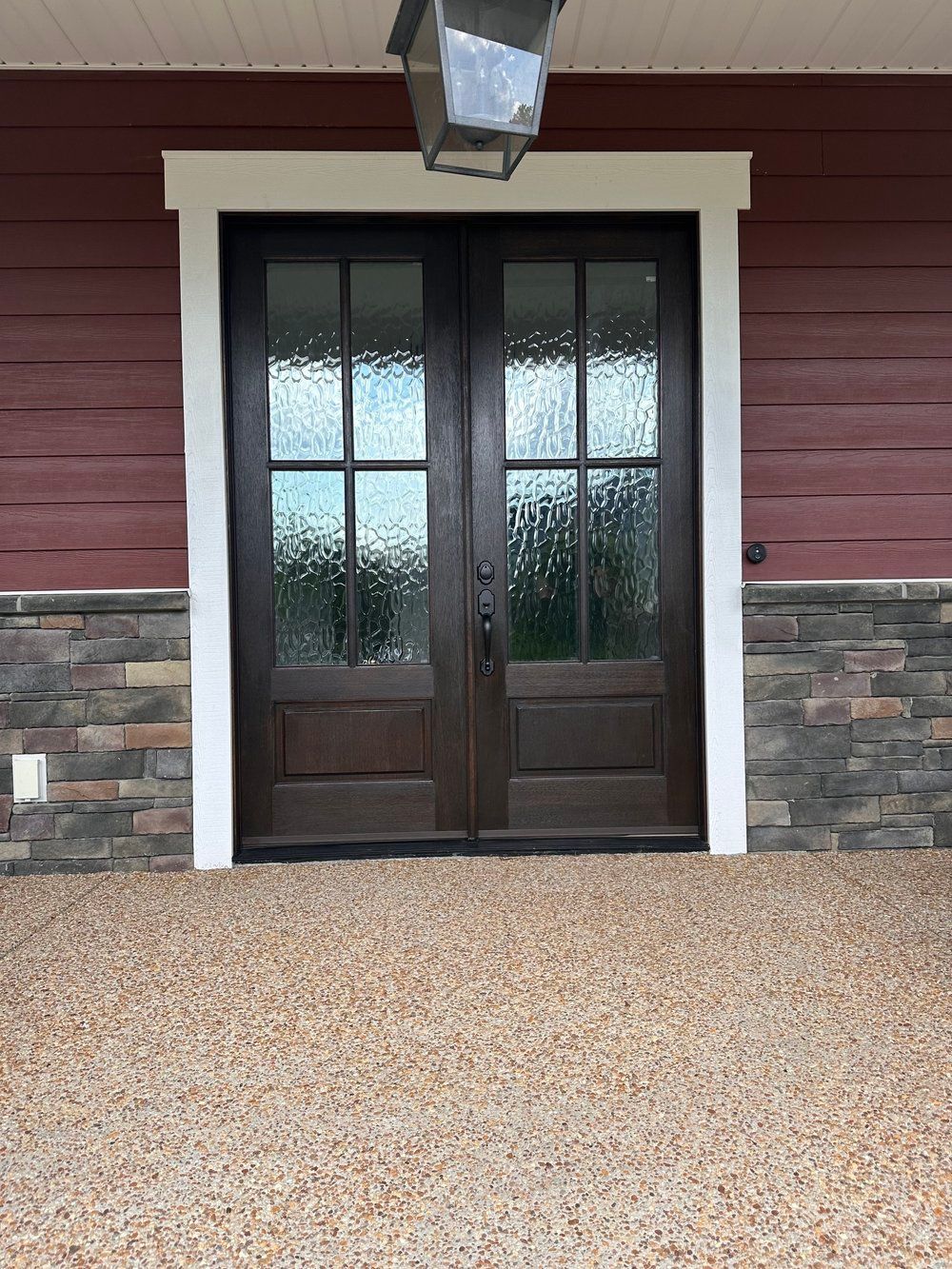 Dark double wooden doors with frosted glass beneath a porch light on a stone-and-red siding exterior