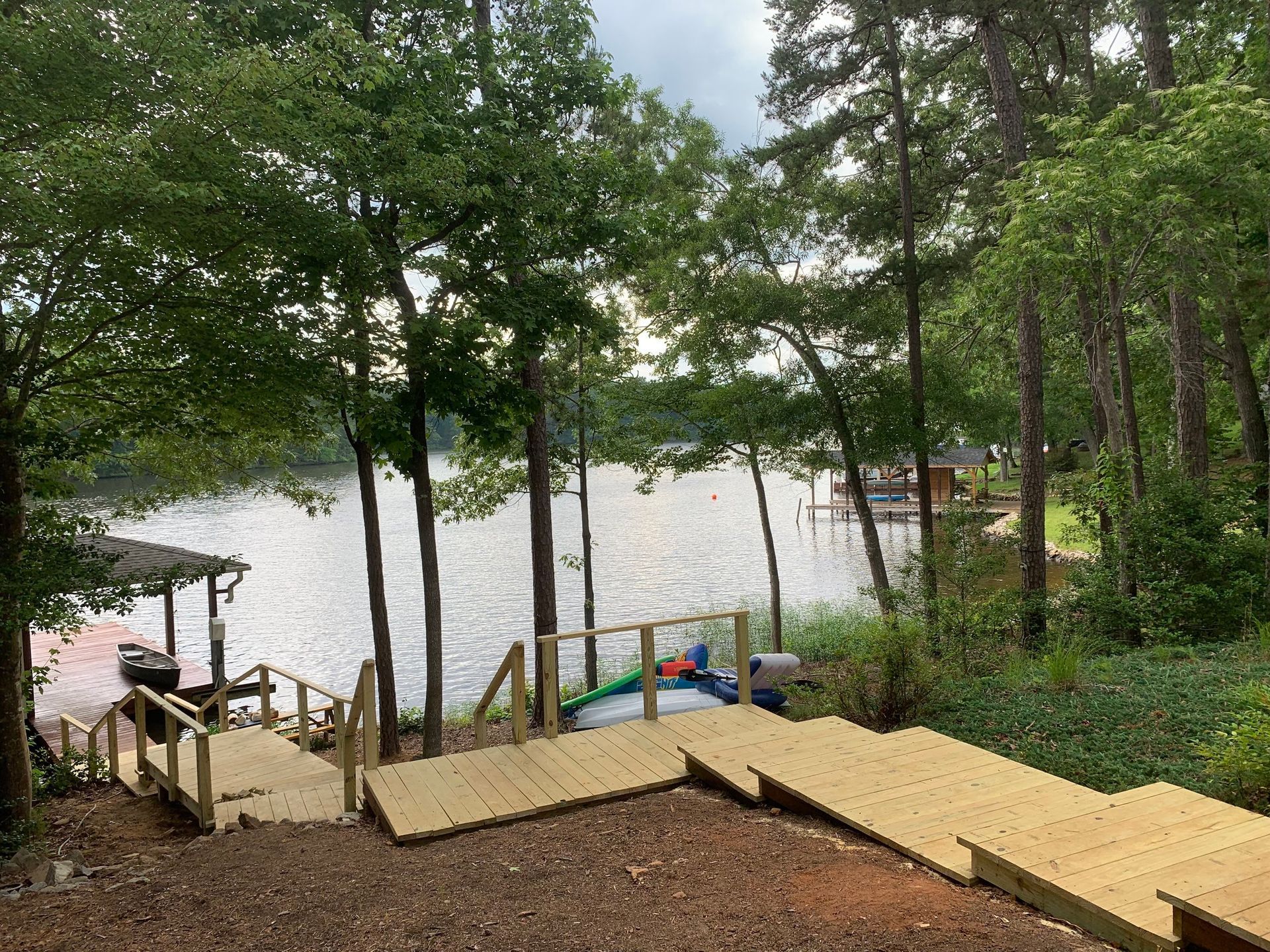 Wooden steps descend to a lakeside dock surrounded by trees and a calm shoreline.