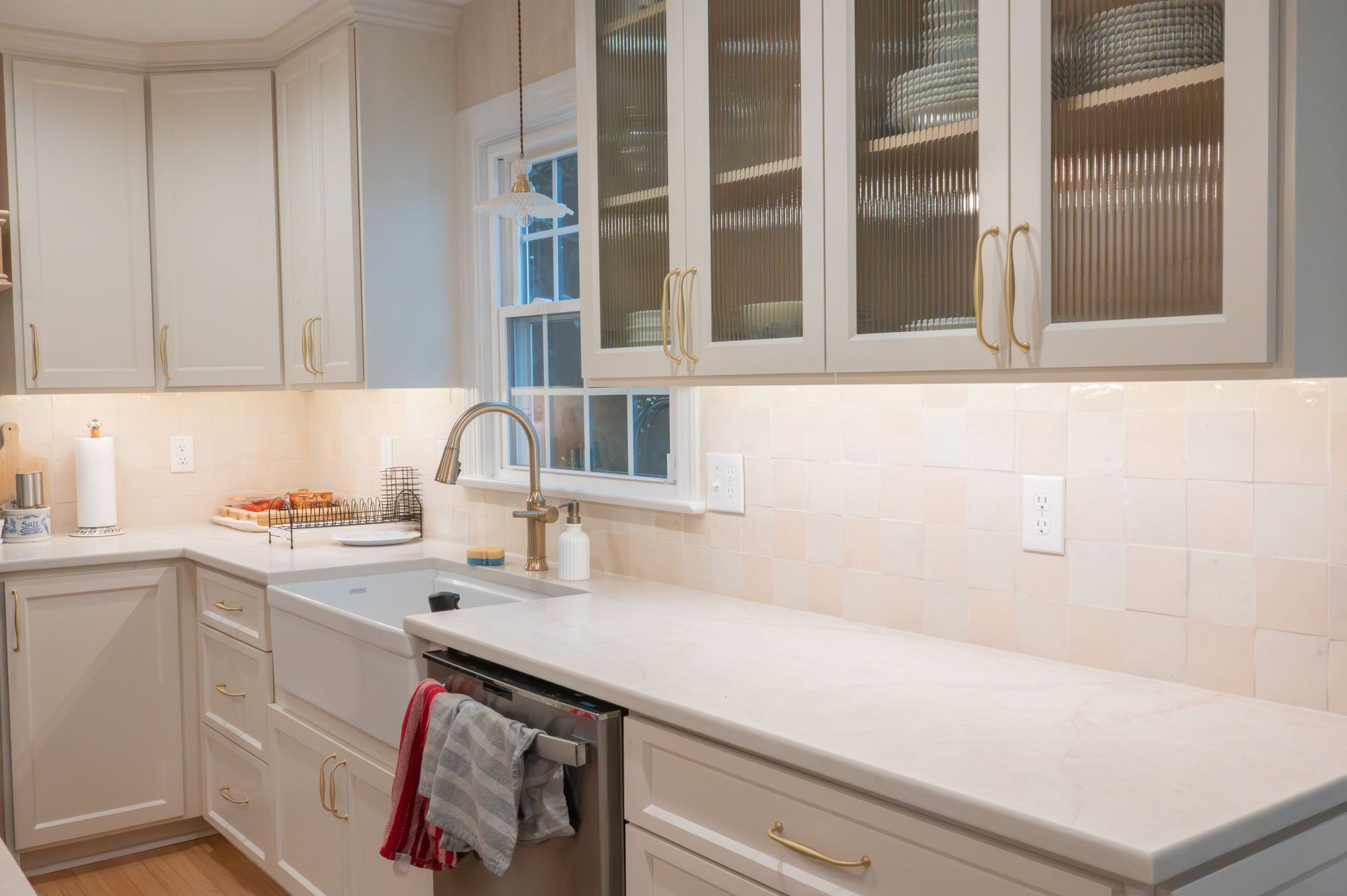 Bright modern kitchen with white cabinets, marble counters, sink, and glass-front upper cupboards