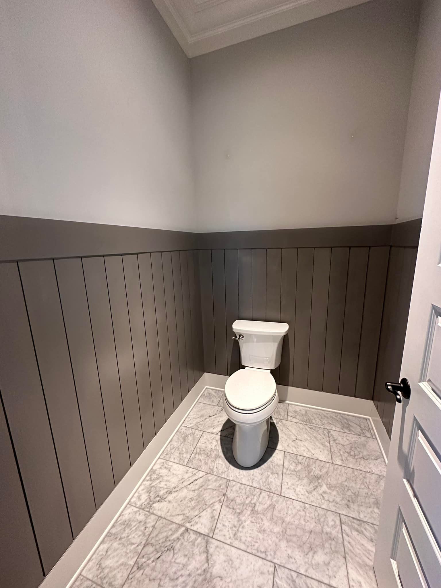 Small bathroom with a toilet against a gray wall and patterned tile floor.