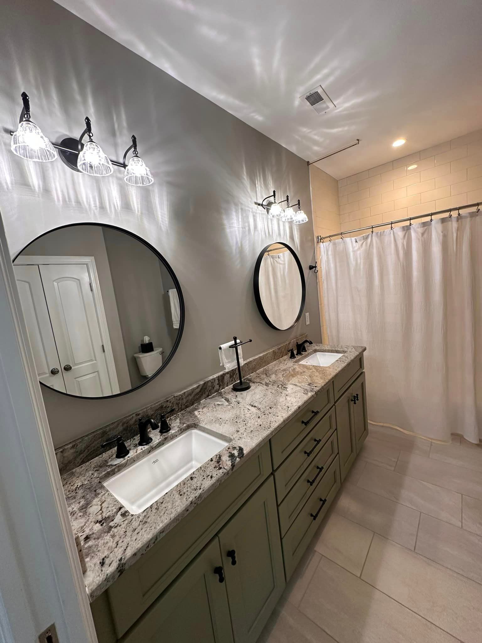 Modern bathroom with olive vanity, marble countertop, round mirrors, wall sconces, and white shower curtain.