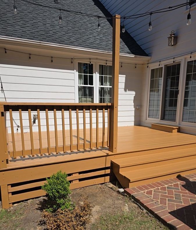 Wooden backyard deck with railing, steps, and string lights beside a house patio.