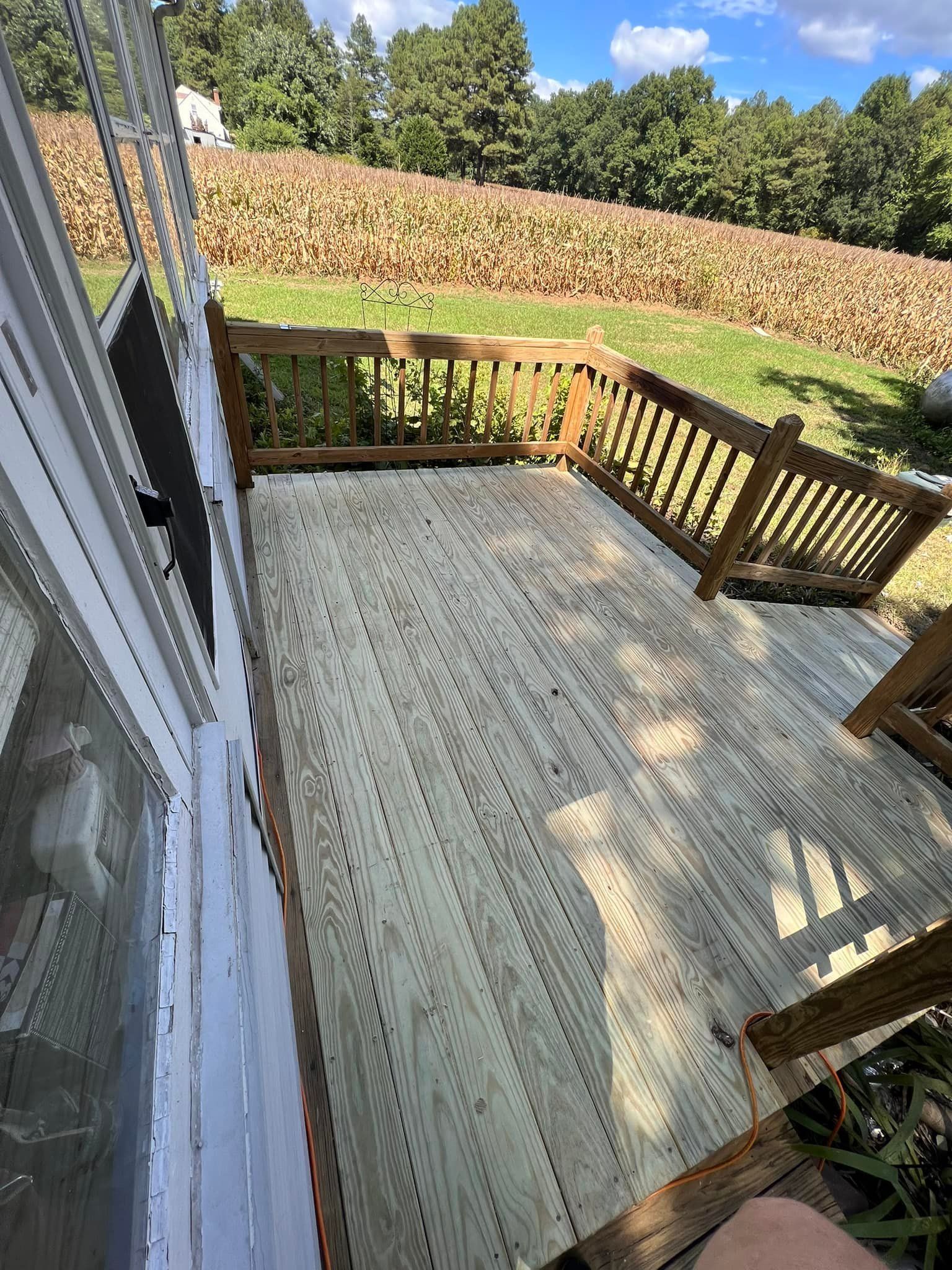 Wooden deck with a light rug, railing, and a view of a grassy yard and trees beyond