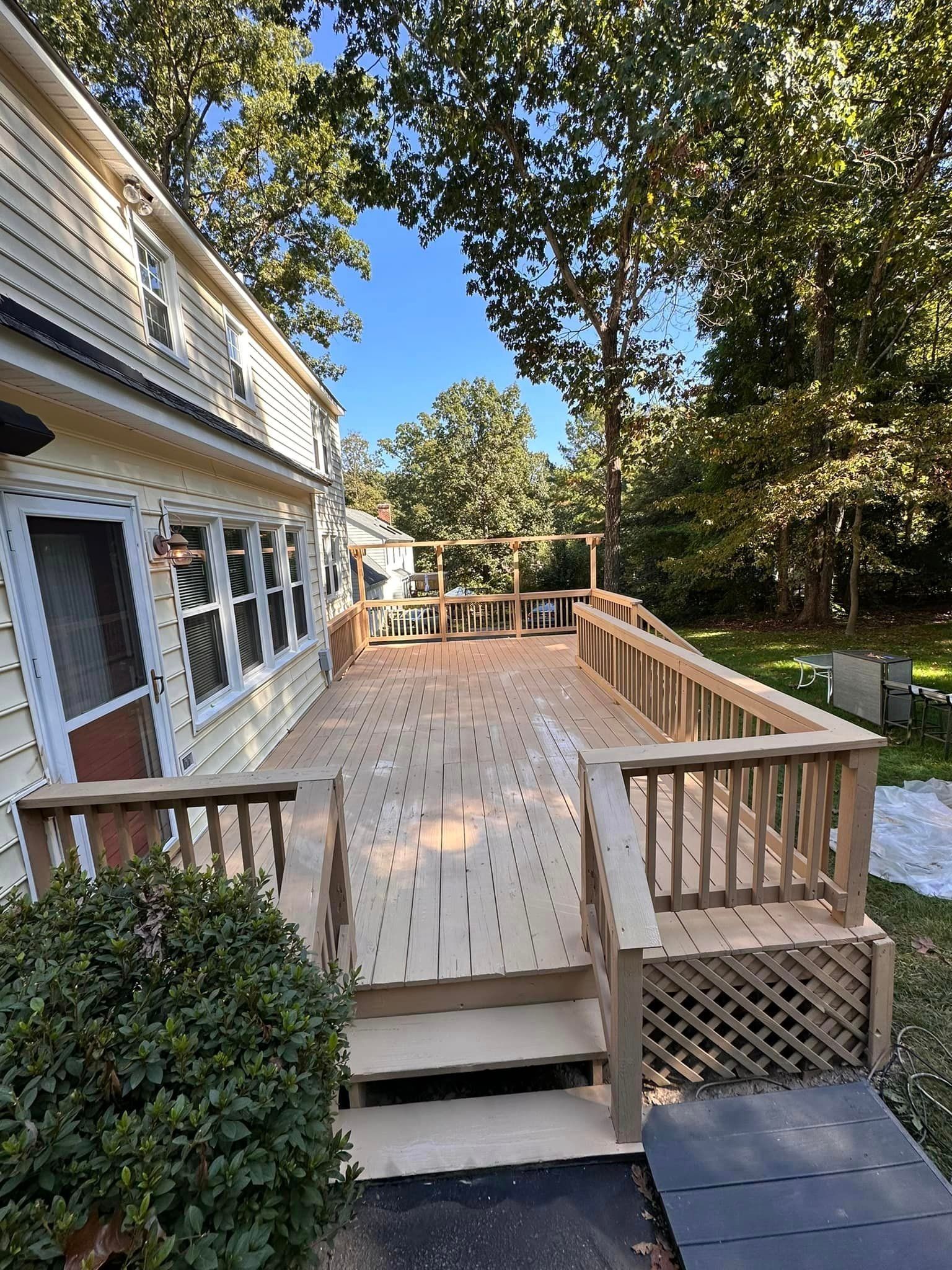 Wooden accessible ramp with railings beside a house, leading to a raised deck under trees.