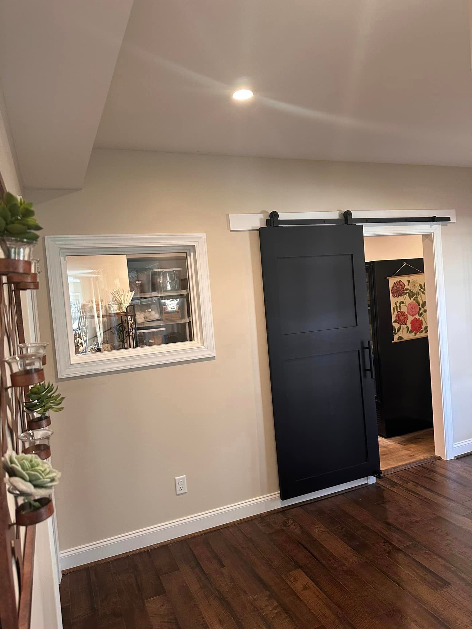 Empty room with dark wood floors, beige walls, black barn door, and a framed mirror on the left wall