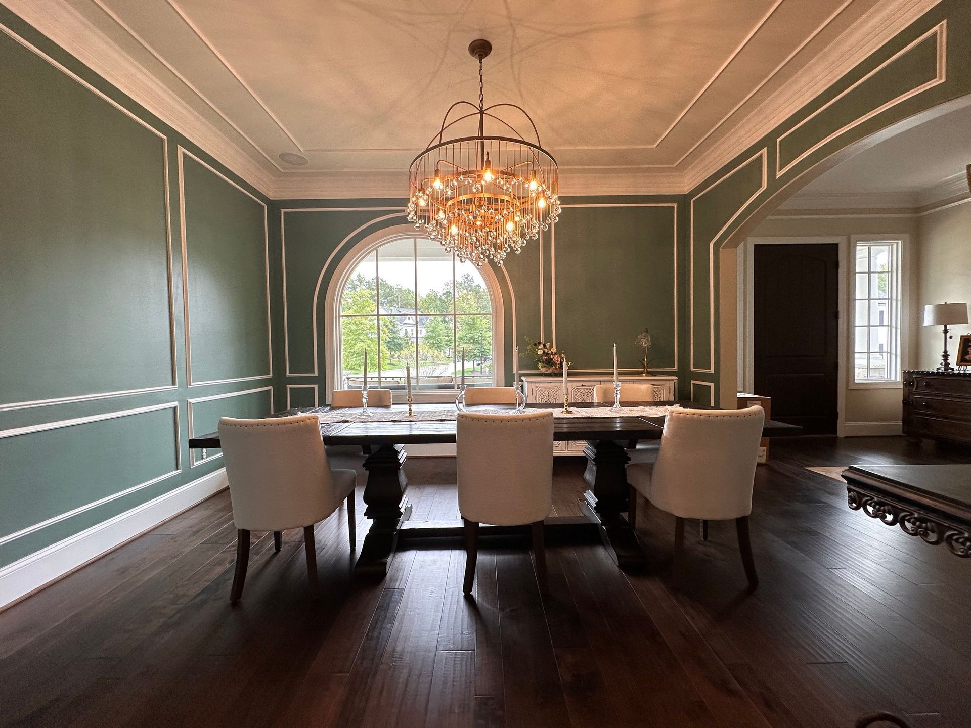Elegant dining room with dark green walls, crystal chandelier, and a large table by a window.