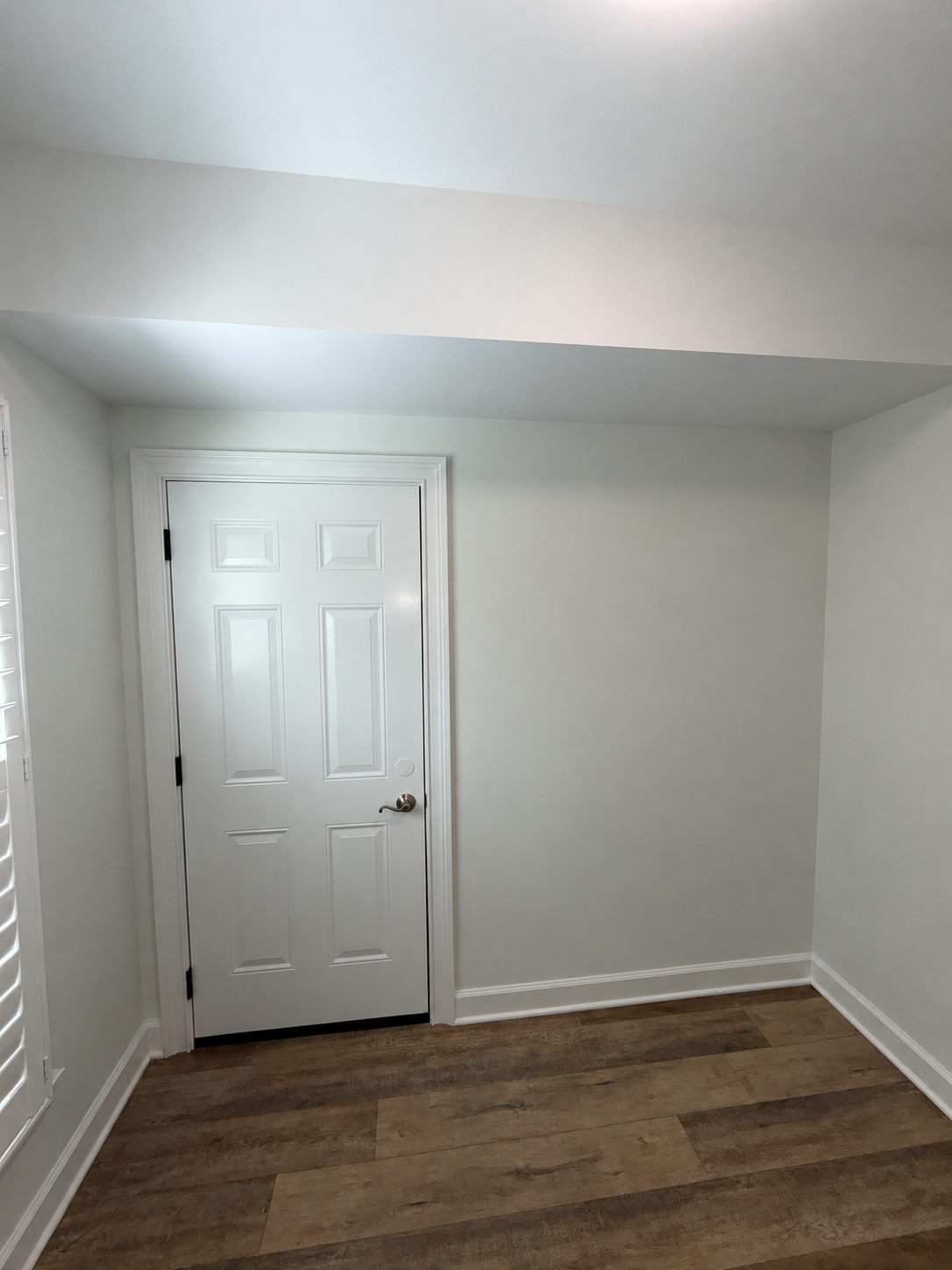 Empty room with white walls, a white door, and wood flooring under a sloped ceiling.