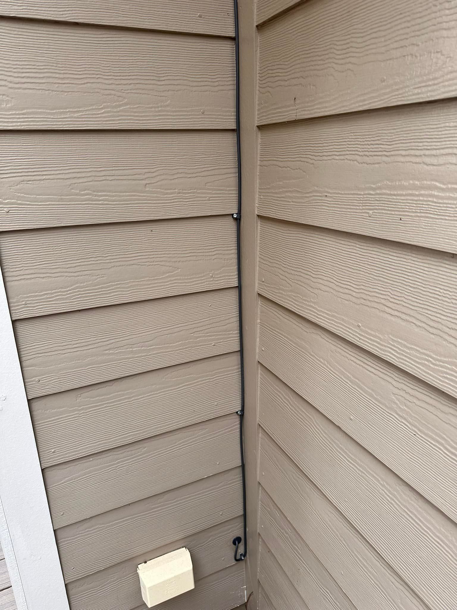 Beige house siding with a small exterior light at the base and a vertical corner seam.