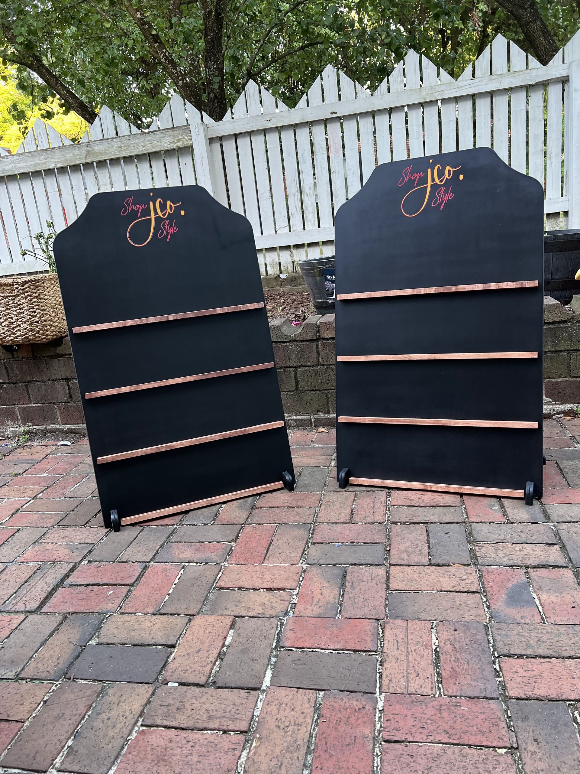 Two black shelves are sitting on a brick sidewalk