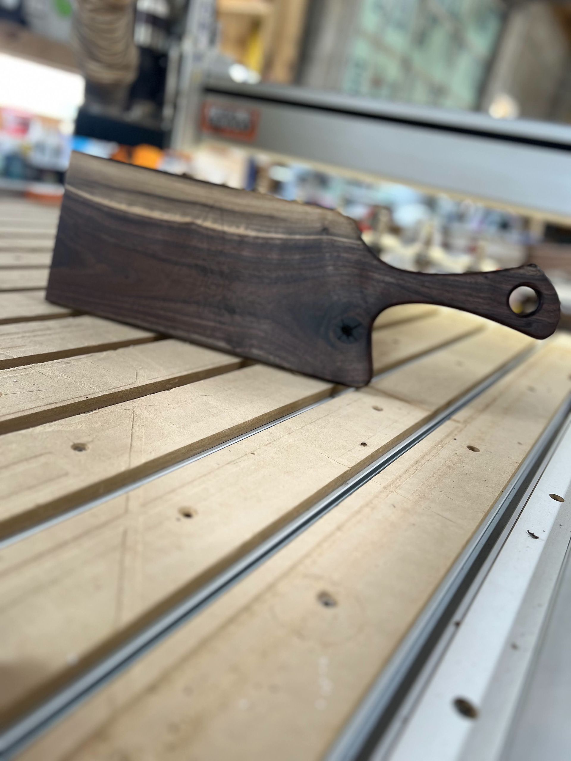 Dark wooden hand tool or blade handle resting on a slatted workbench in a workshop.