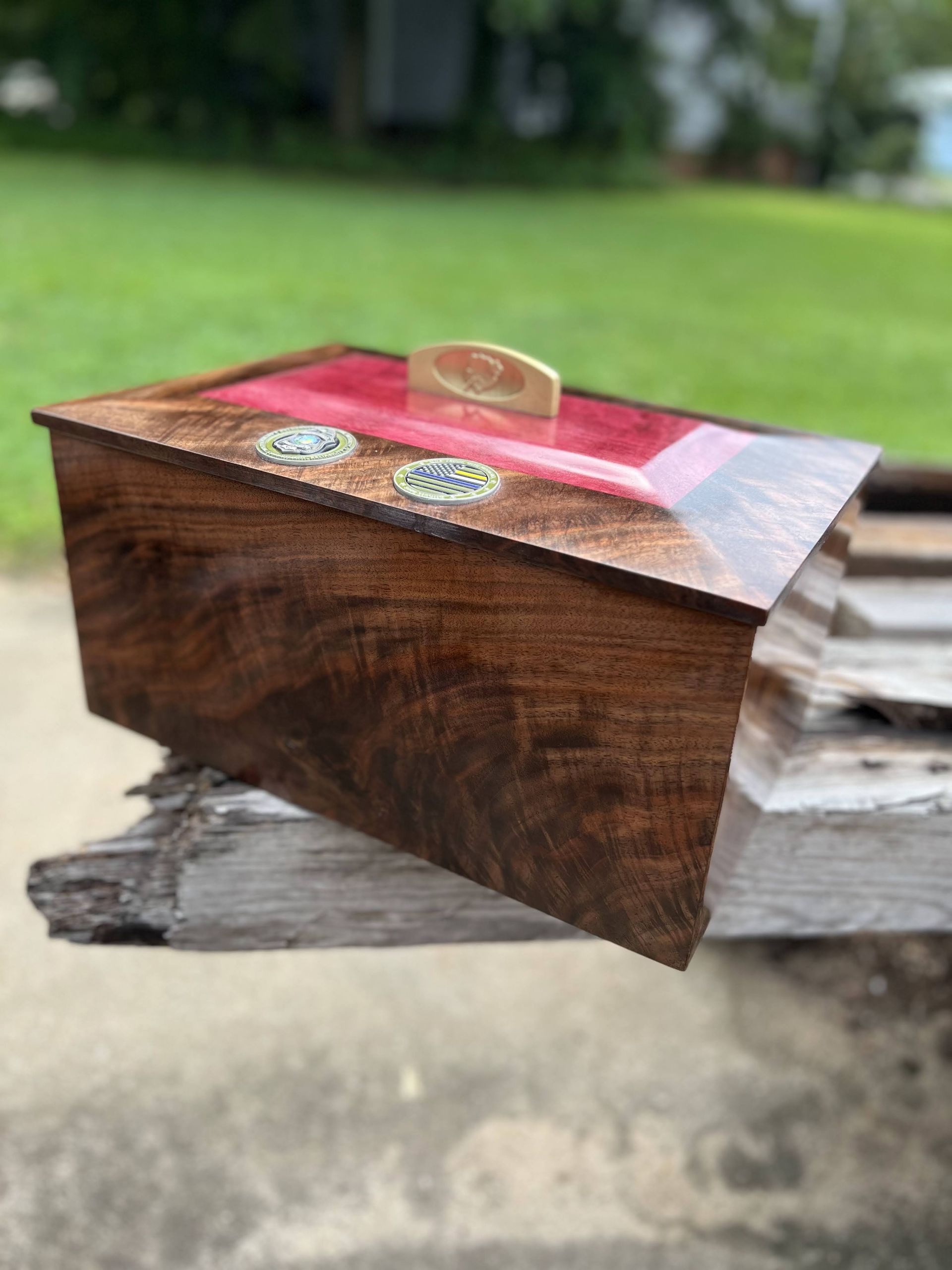 Small wooden keepsake box with pink top and a brass handle, resting on a rustic log outdoors.