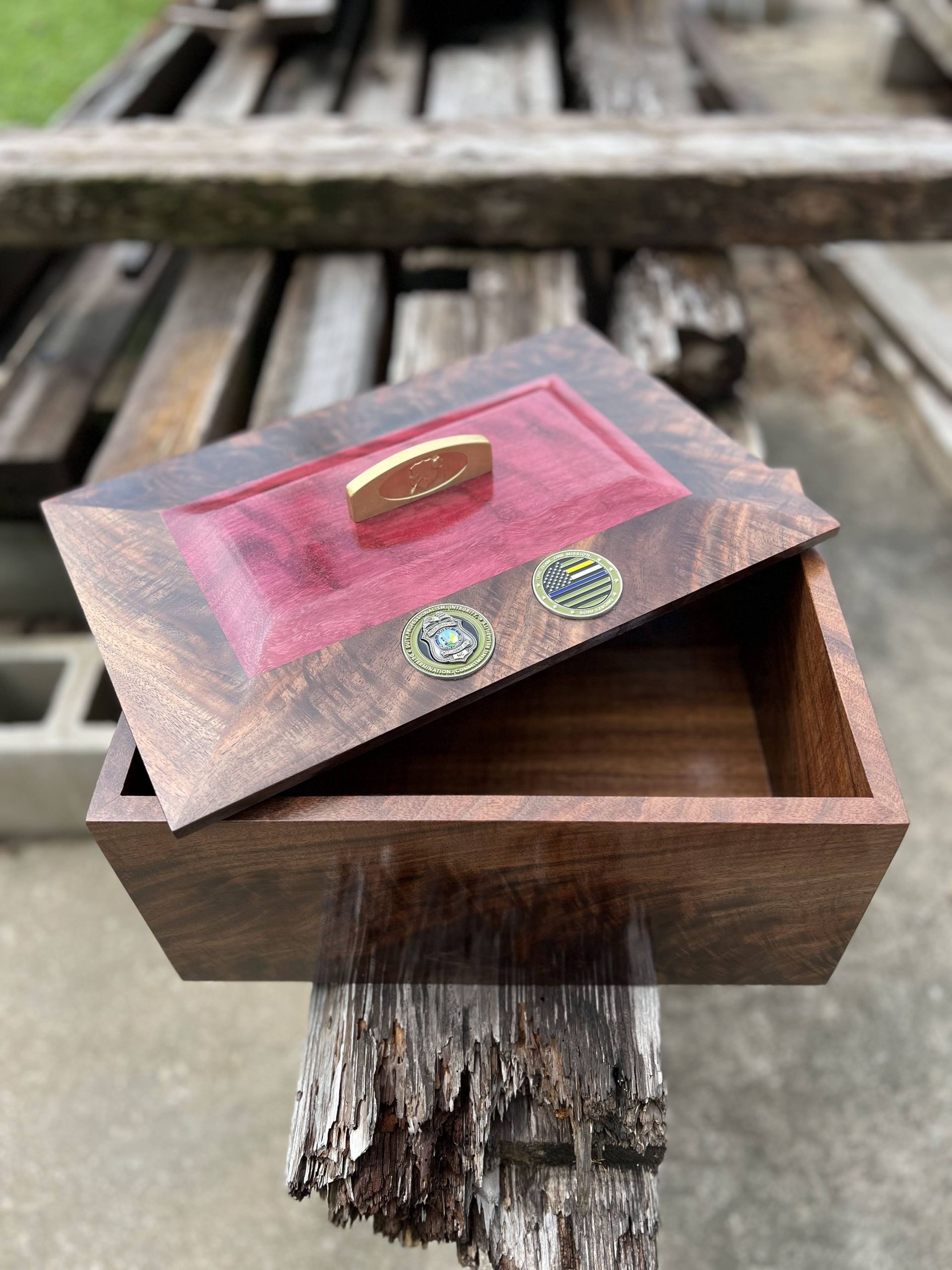 Small wooden box with a hinged lid and handle, resting on a weathered wooden surface outdoors.