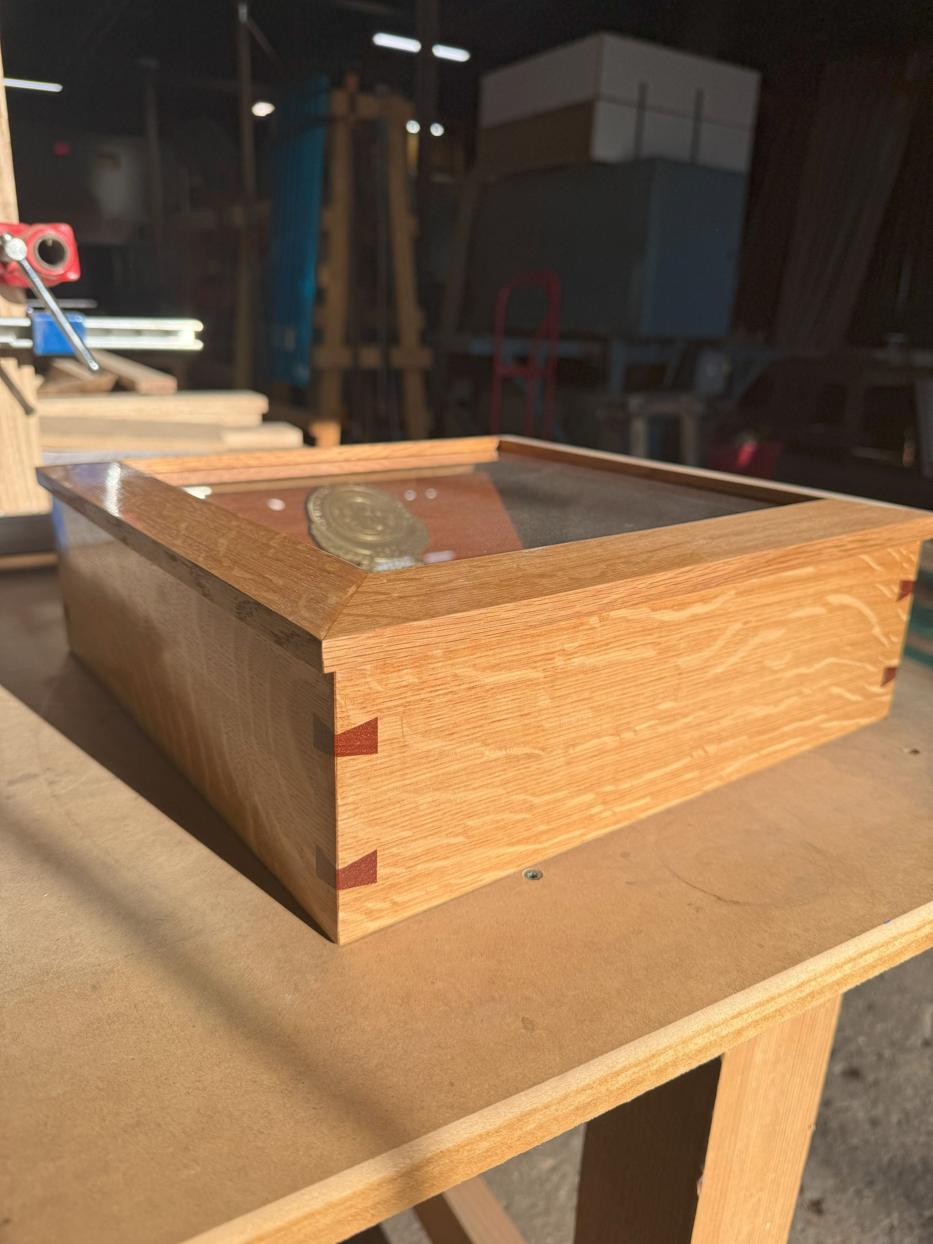 Wooden box on a workbench in a dim workshop, with a coin resting on top.
