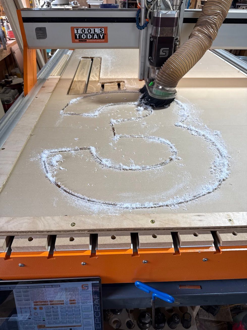 CNC router cutting a circular design into wood, with sawdust scattered on the worktable.