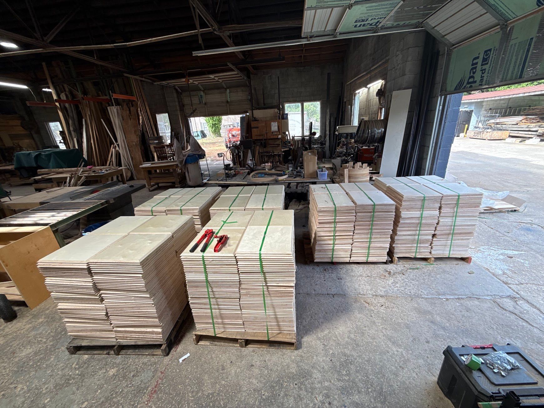 Stacks of white tiles or boards on pallets inside an industrial warehouse, with an open bay door.