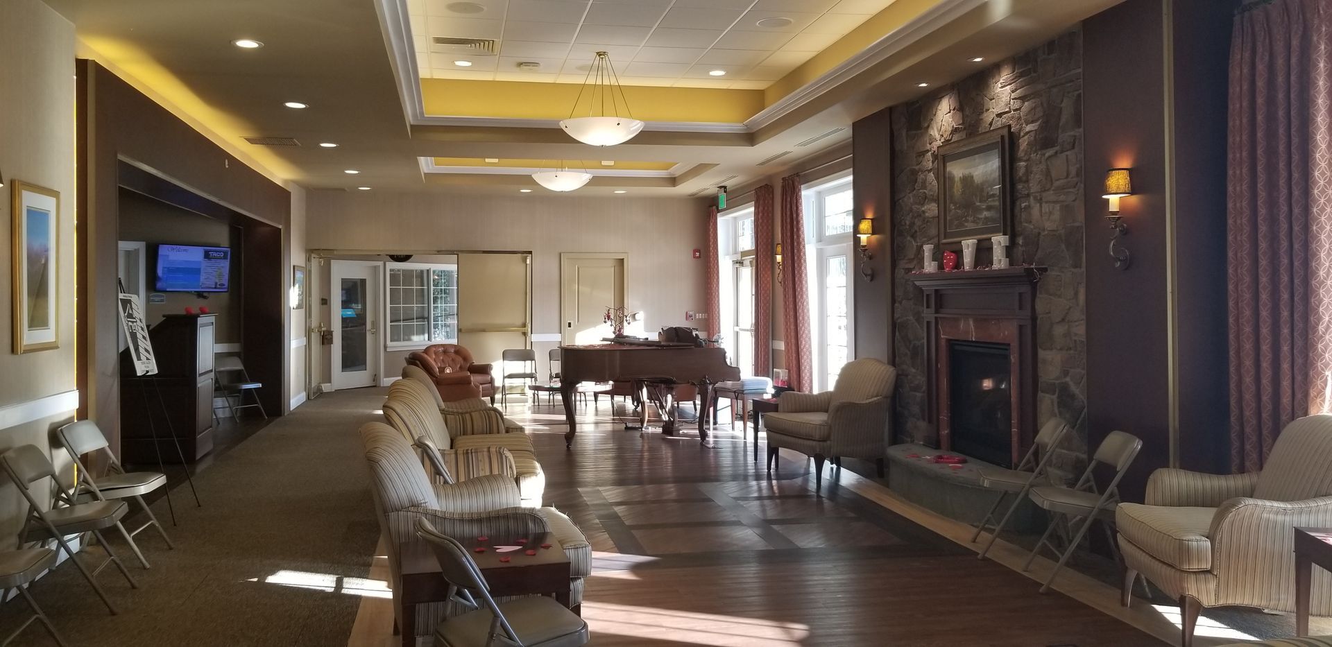 Long hallway with seating, fireplace, piano, and doors. Warm lighting.