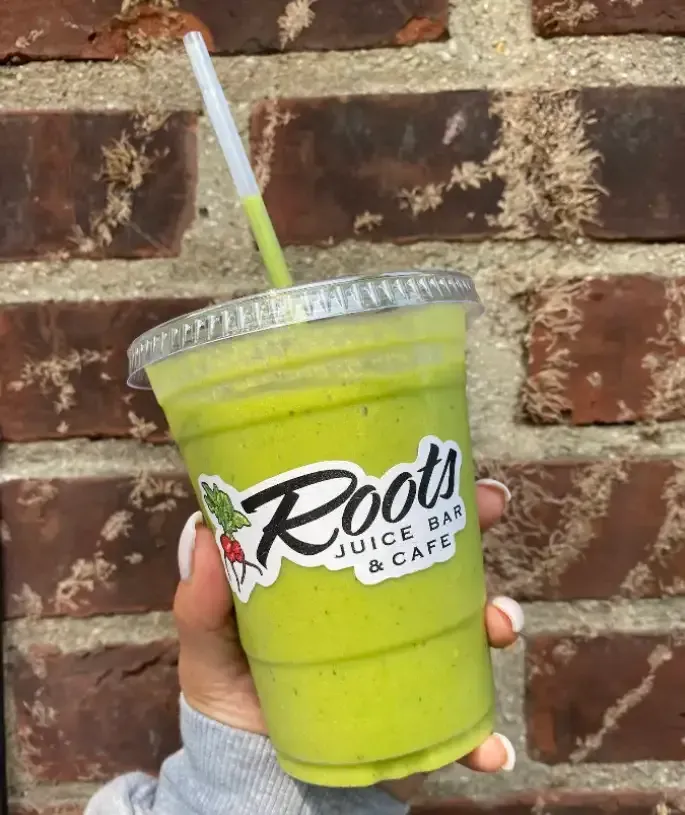 Green smoothie in a clear cup from Roots Smoothies Juices & Acai Bowls outdoors