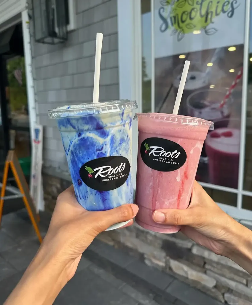 Two hands holding blue and pink smoothie cups outside a shop
