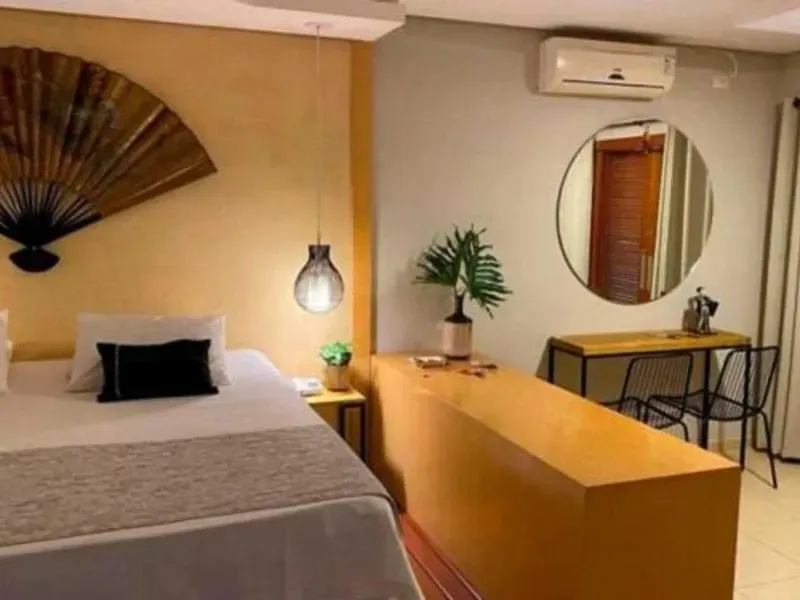 Um quarto com uma cama com um grande ventilador de parede, uma escrivaninha minimalista com duas cadeiras e um espelho redondo.