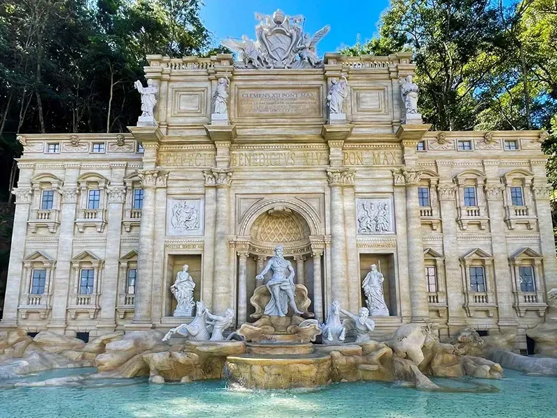 Uma réplica em escala da Fontana di Trevi, em Roma, com arquitetura ornamentada em pedra, estátuas clássicas e uma bacia de água azul.