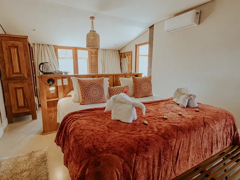 Um quarto aconchegante com cabeceira de madeira, um grande cobertor laranja e uma toalha dobrada em forma de elefante sobre a cama.