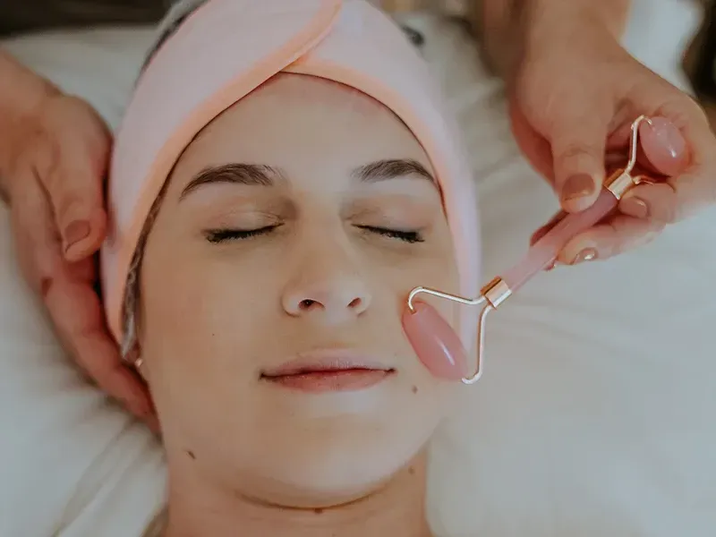 Uma pessoa recebe uma massagem facial com um rolo de jade rosa enquanto usa uma faixa de cabeça macia cor pêssego.
