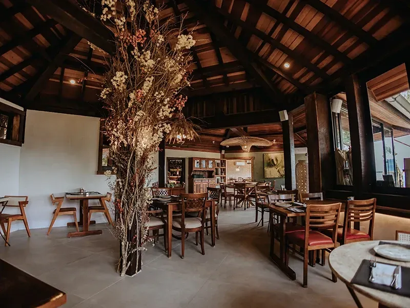 Interior de restaurante rústico com iluminação suave, tetos abobadados de madeira, móveis de madeira e uma grande planta seca no centro.