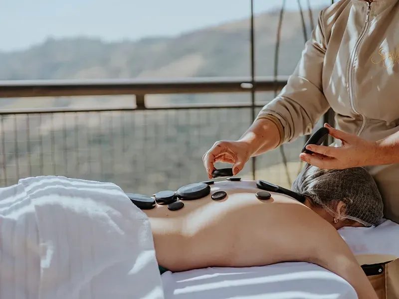 Uma pessoa recebendo uma massagem com pedras quentes nas costas, com um terapeuta colocando pedras pretas lisas sobre sua pele.