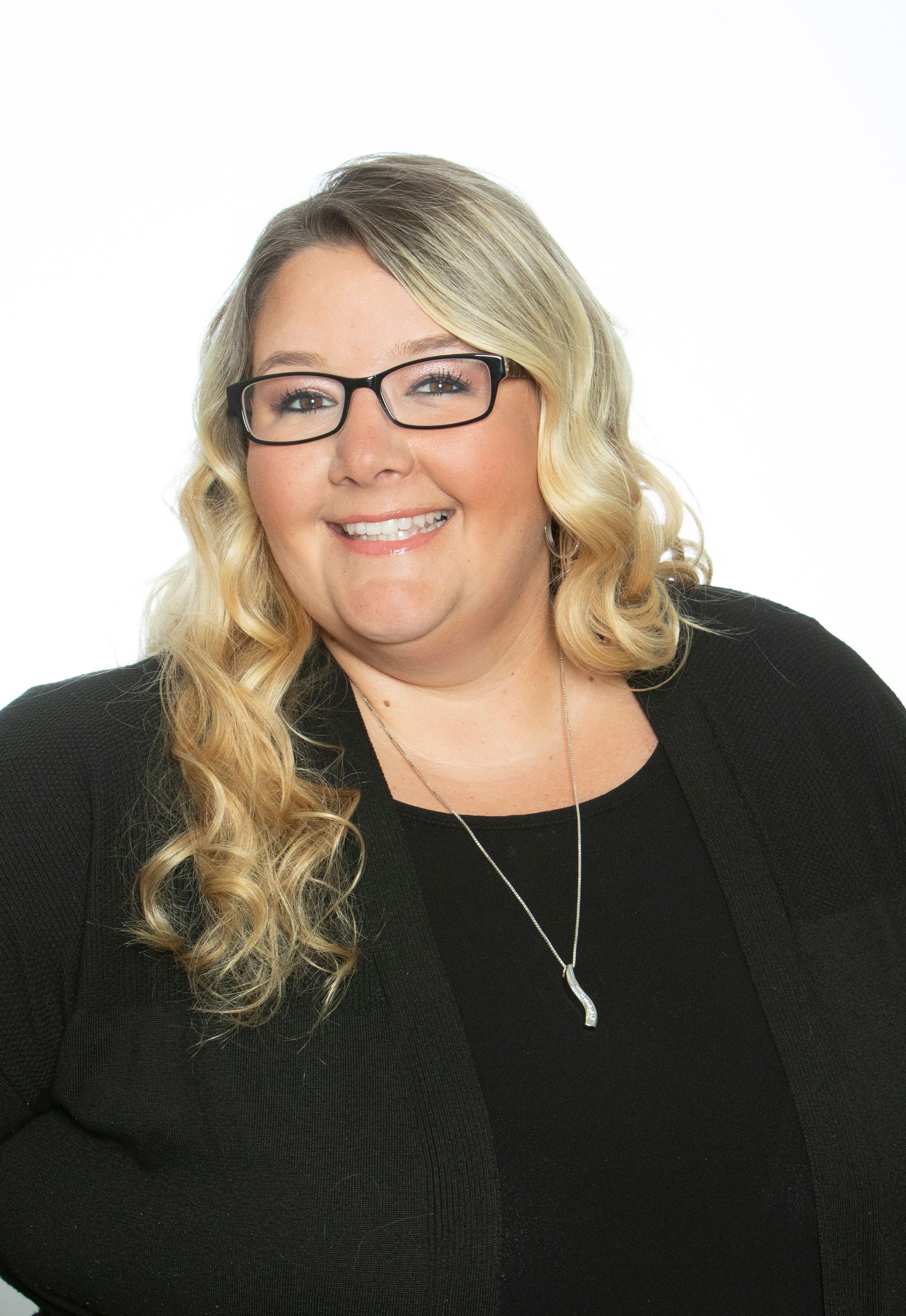 A woman wearing glasses and a black jacket is smiling for the camera.
