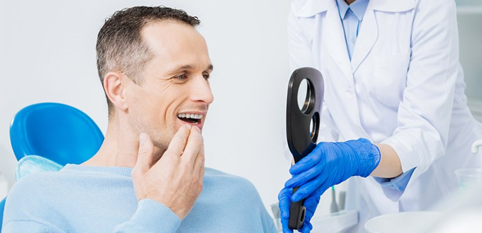 A man is sitting in a dental chair looking at his teeth in a mirror.
