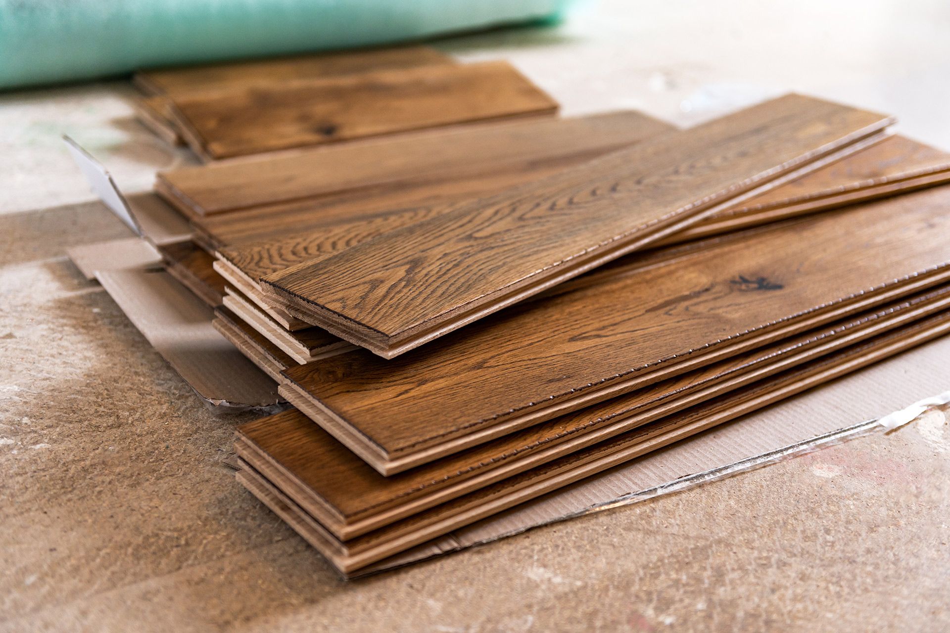 Stack of brown wooden planks on a work surface, with a green roll in the background.